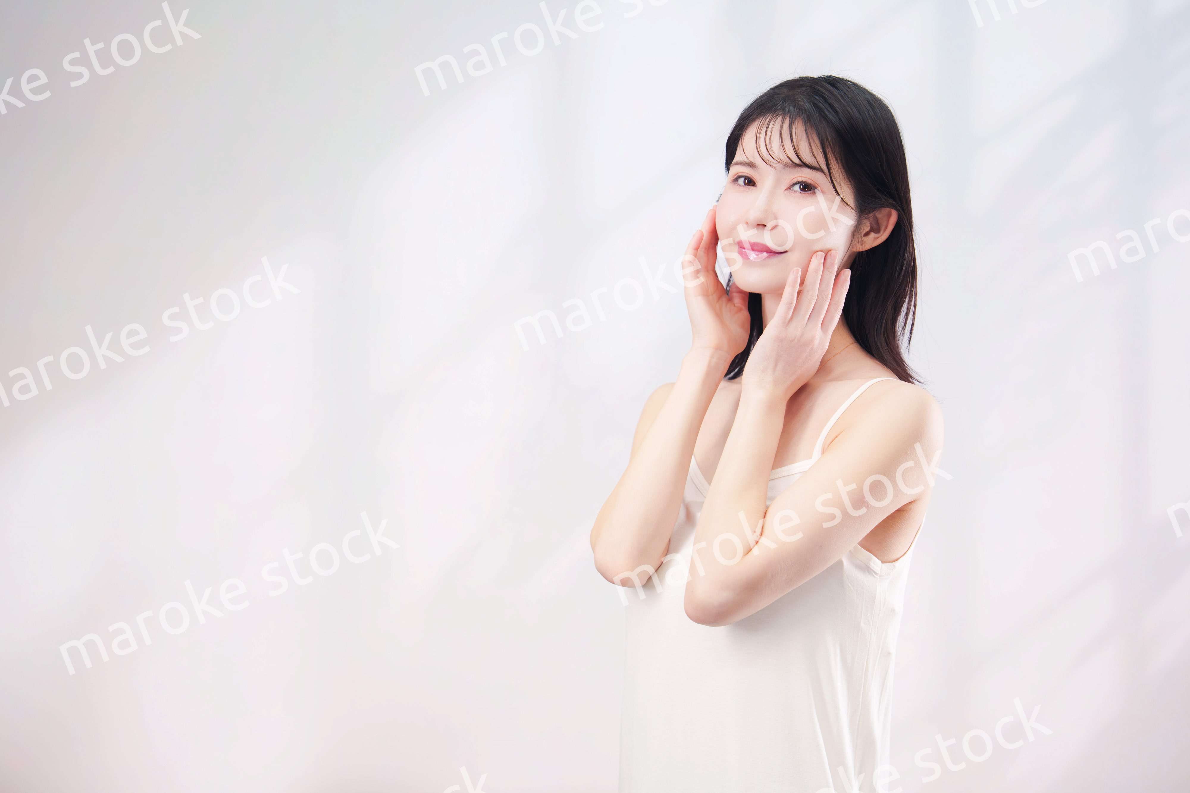 笑顔でお肌のケアをする若い女性（シンプル背景）