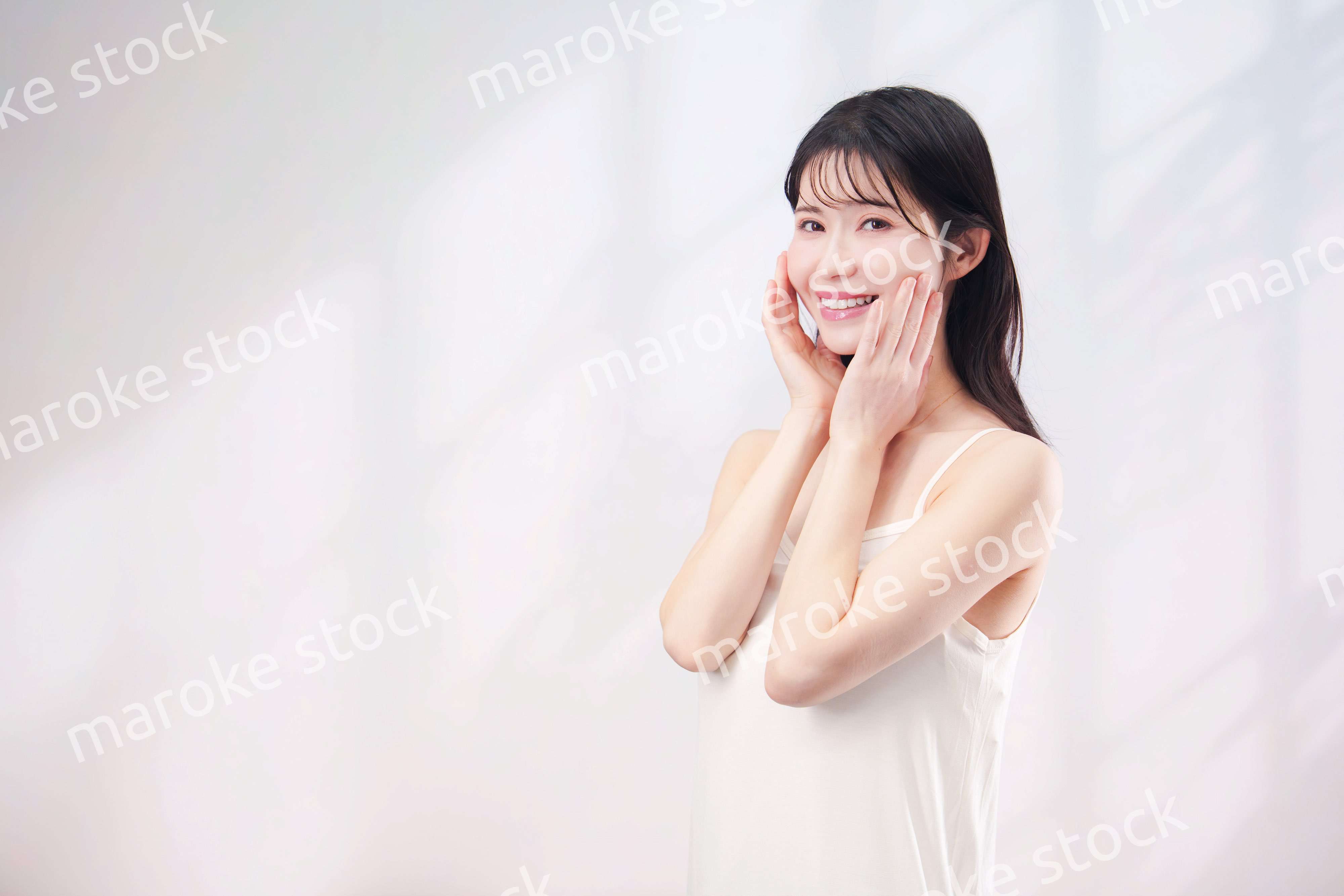 笑顔でお肌のケアをする若い女性（シンプル背景）