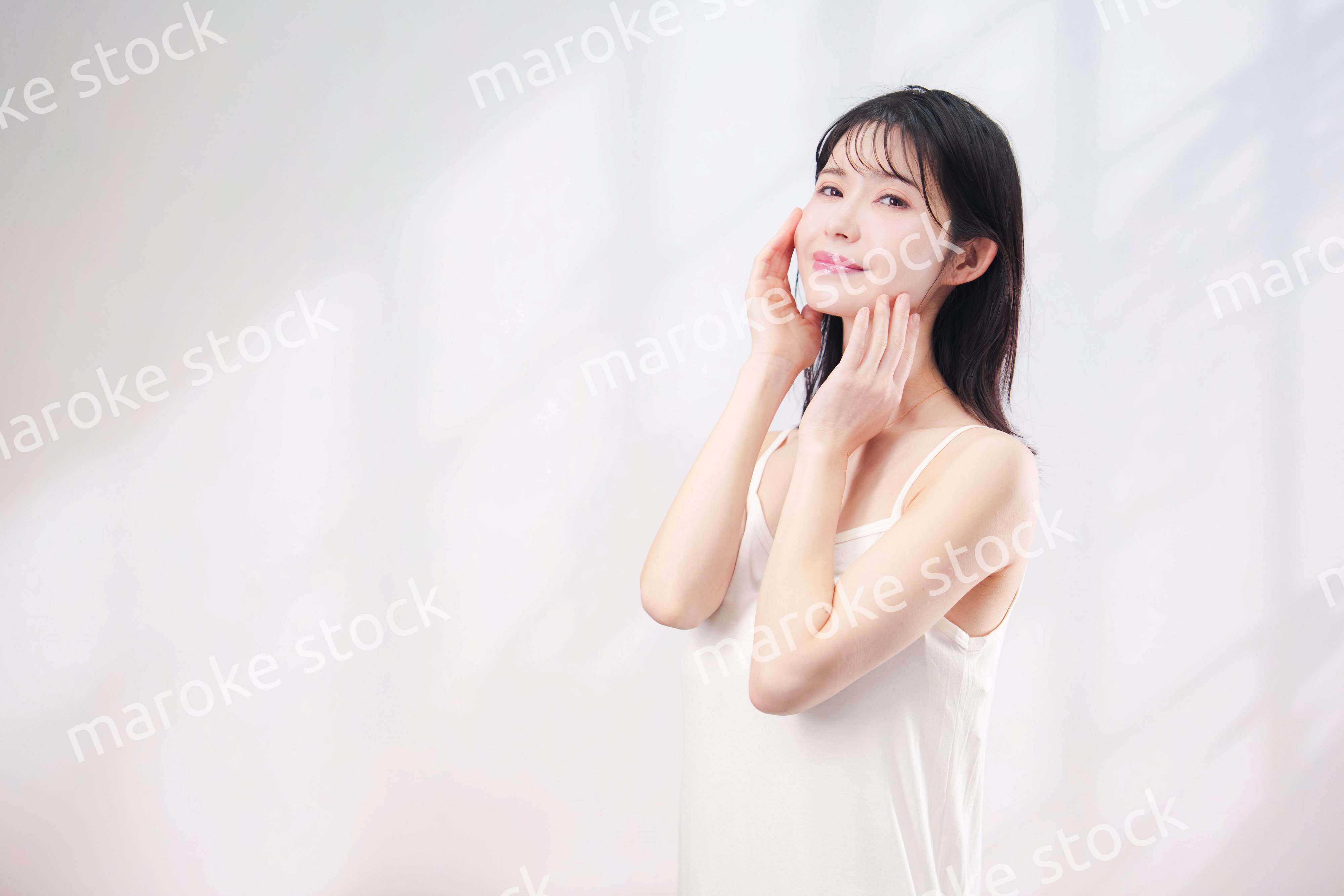 笑顔でお肌のケアをする若い女性（シンプル背景）