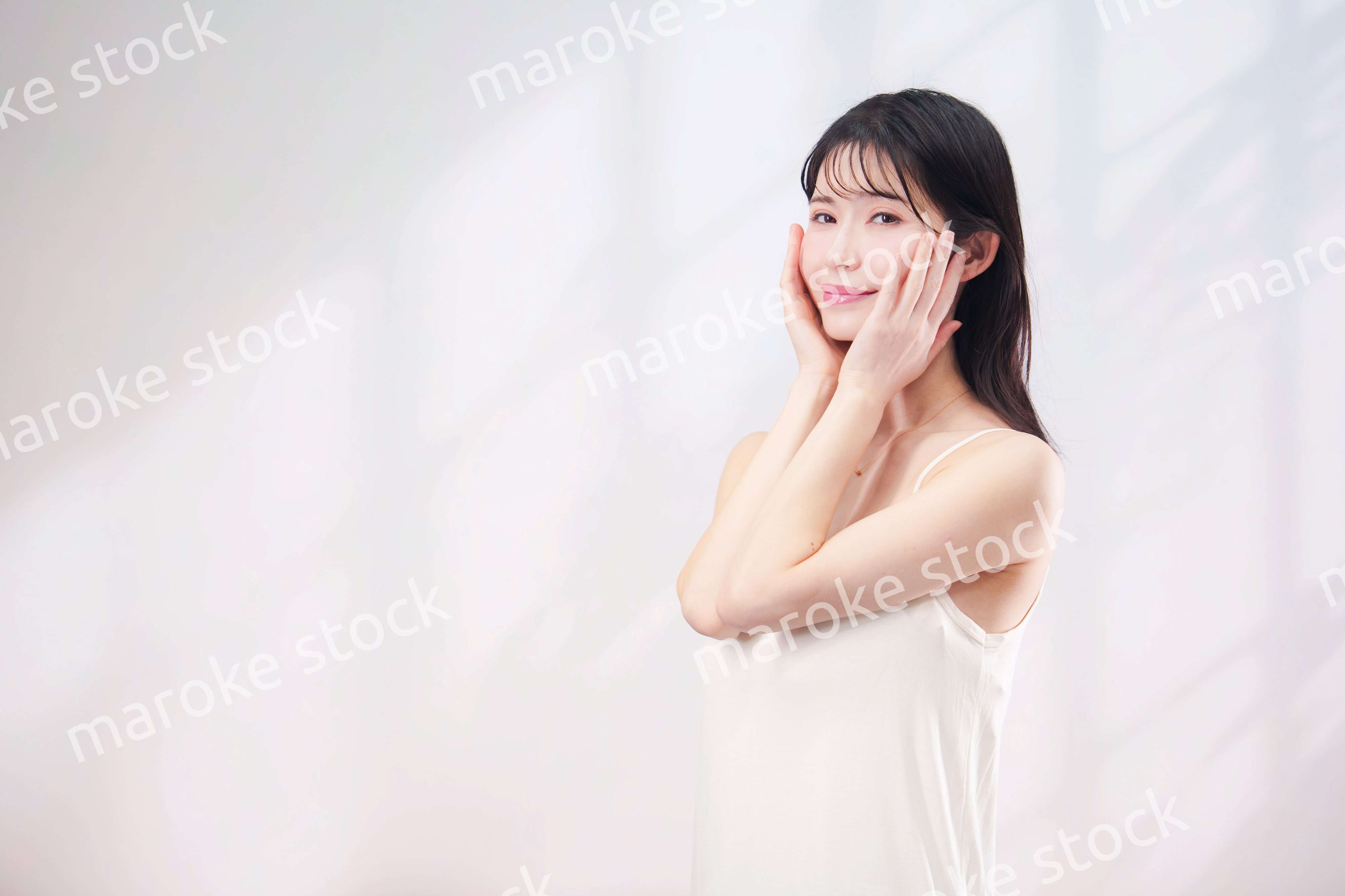 笑顔でお肌のケアをする若い女性（シンプル背景）