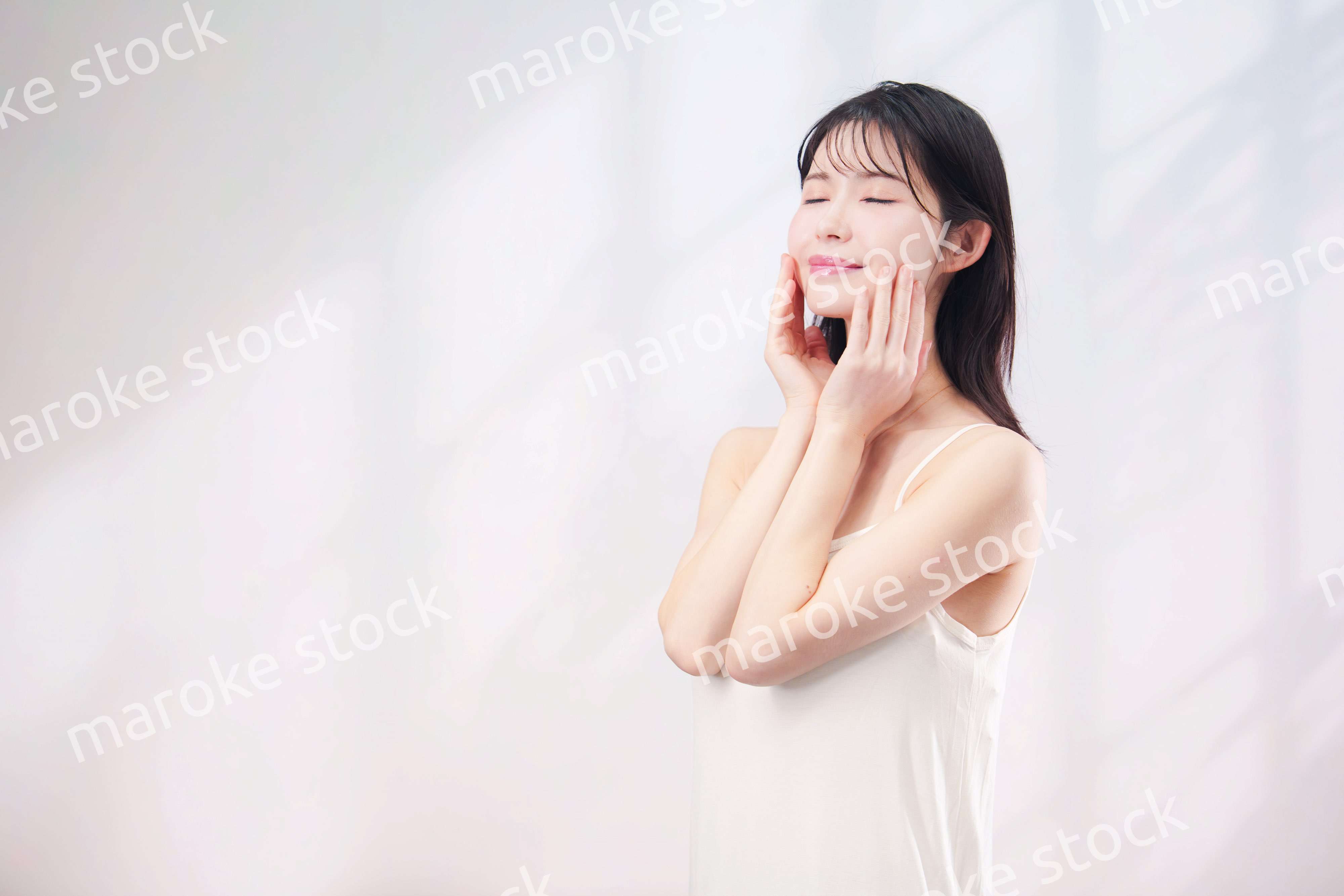 笑顔でお肌のケアをする若い女性（シンプル背景）