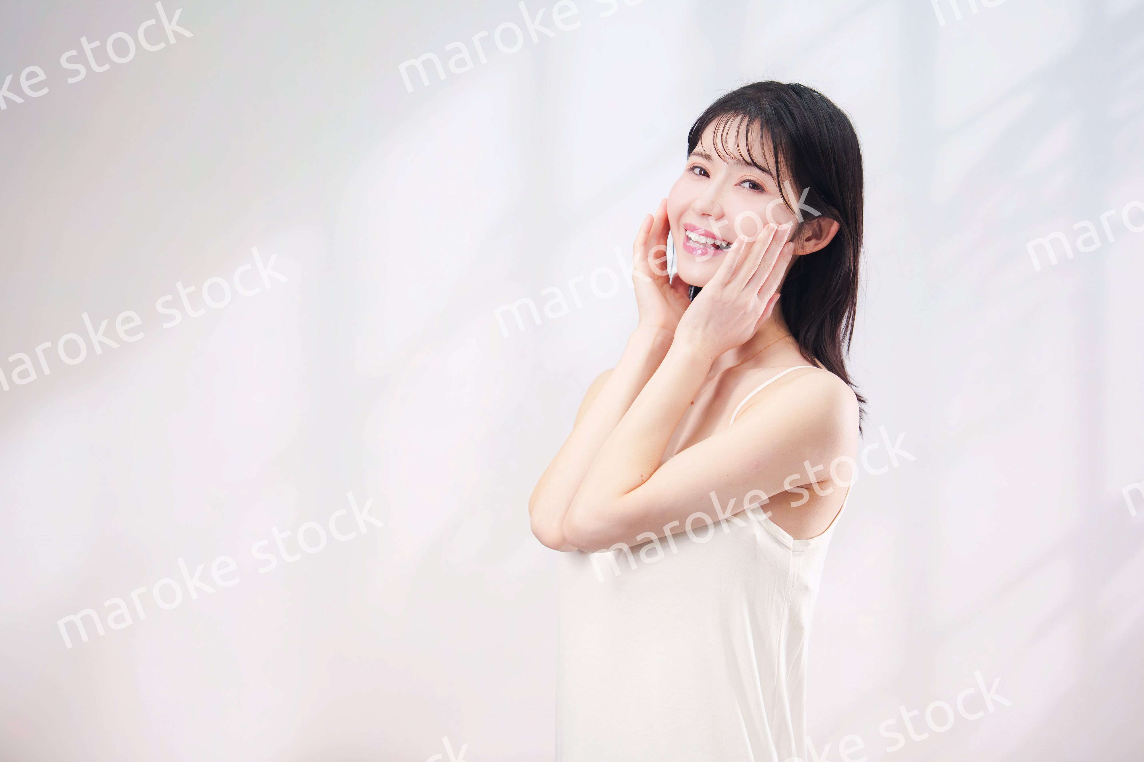 笑顔でお肌のケアをする若い女性（シンプル背景）