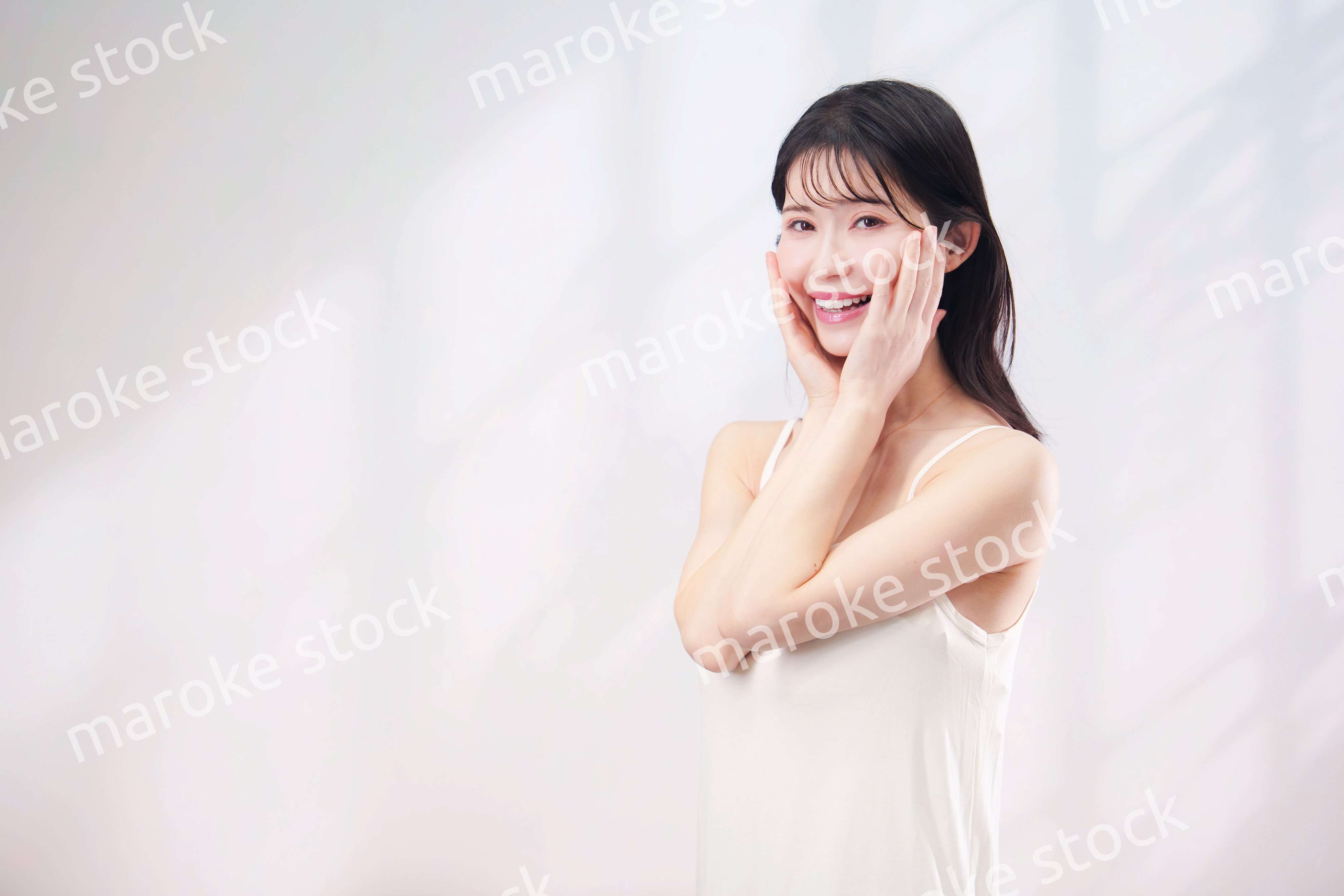 笑顔でお肌のケアをする若い女性（シンプル背景）