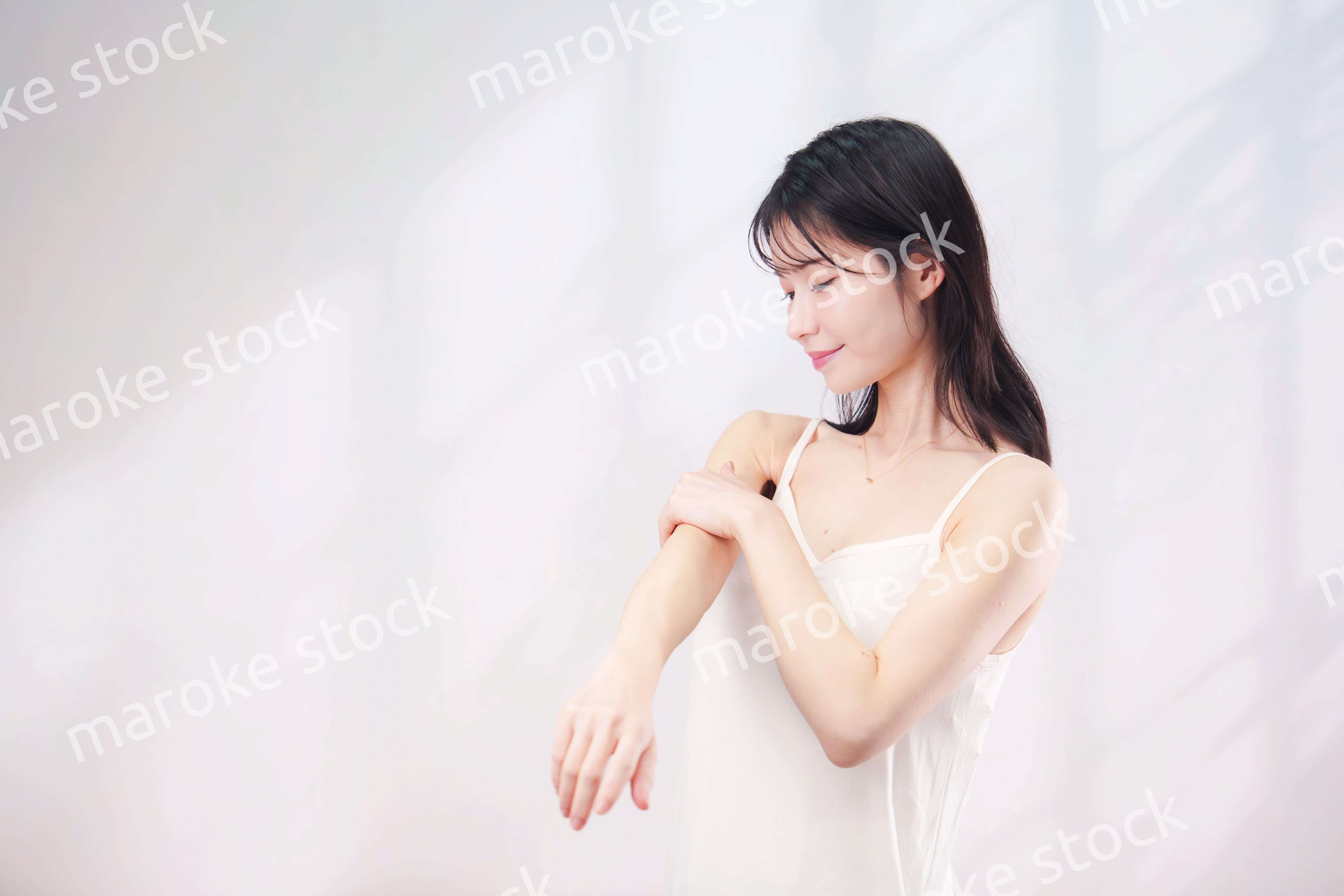 腕にクリームを塗る若い女性（シンプル背景）