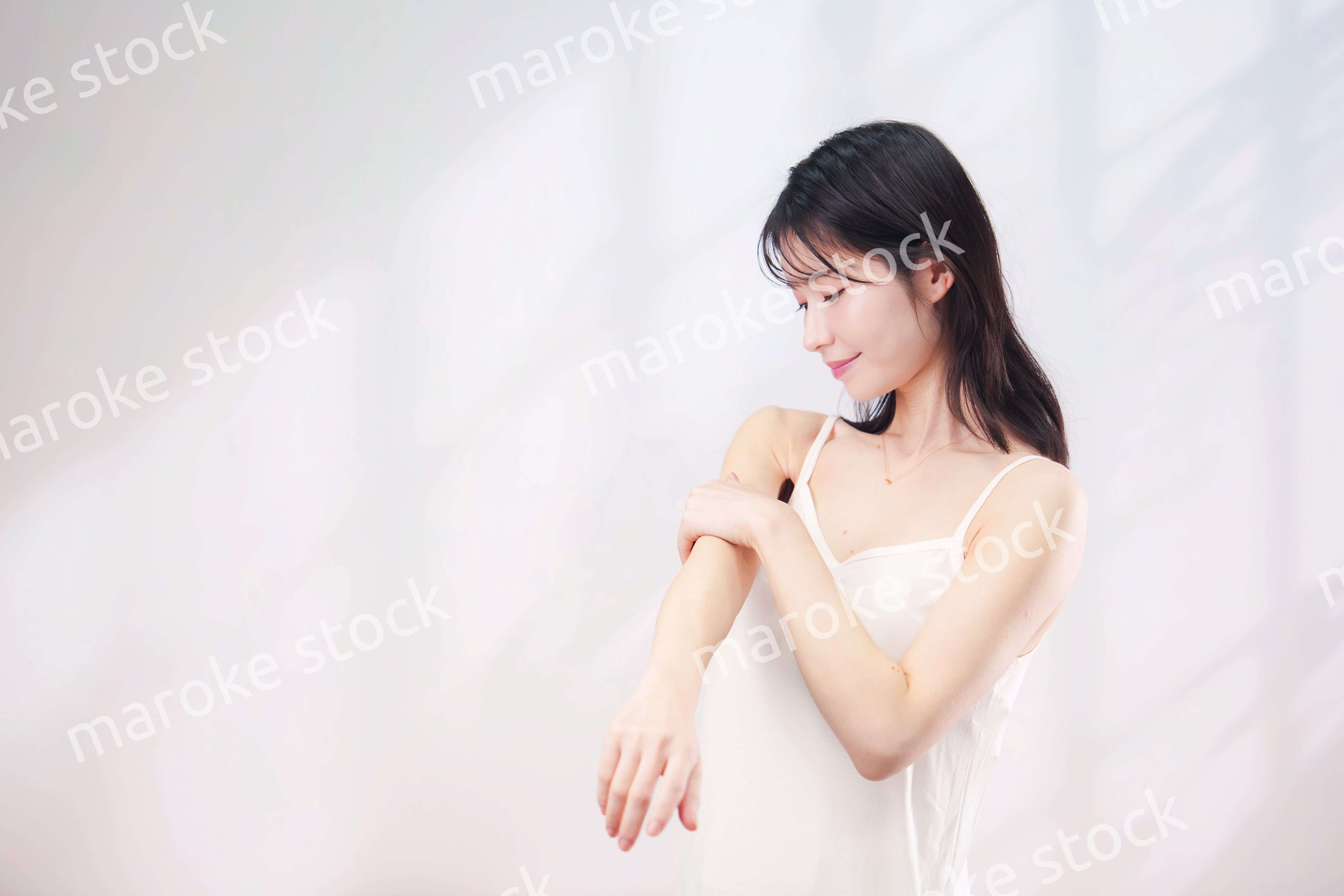 腕にクリームを塗る若い女性（シンプル背景）