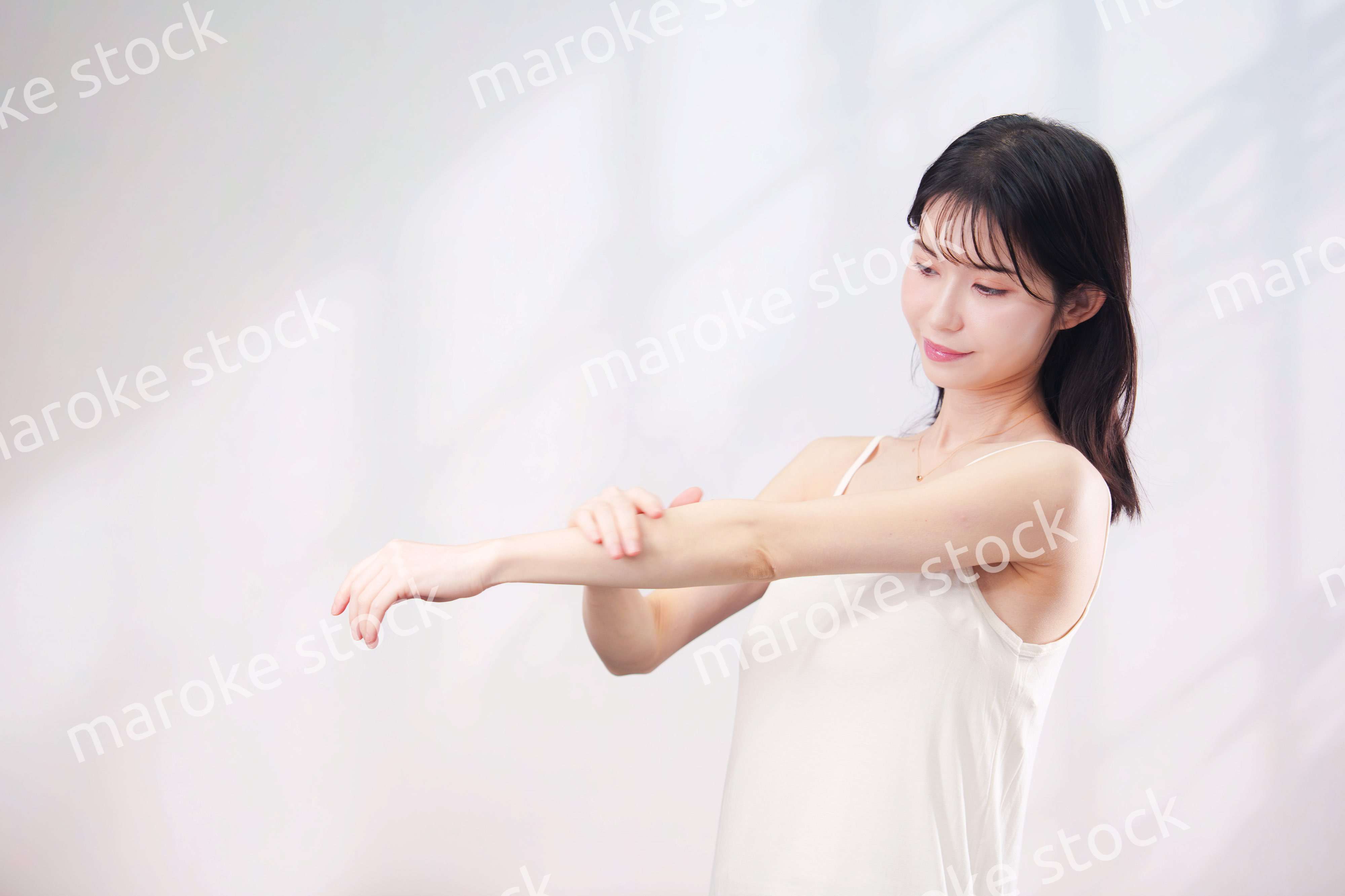 腕にクリームを塗る若い女性（シンプル背景）