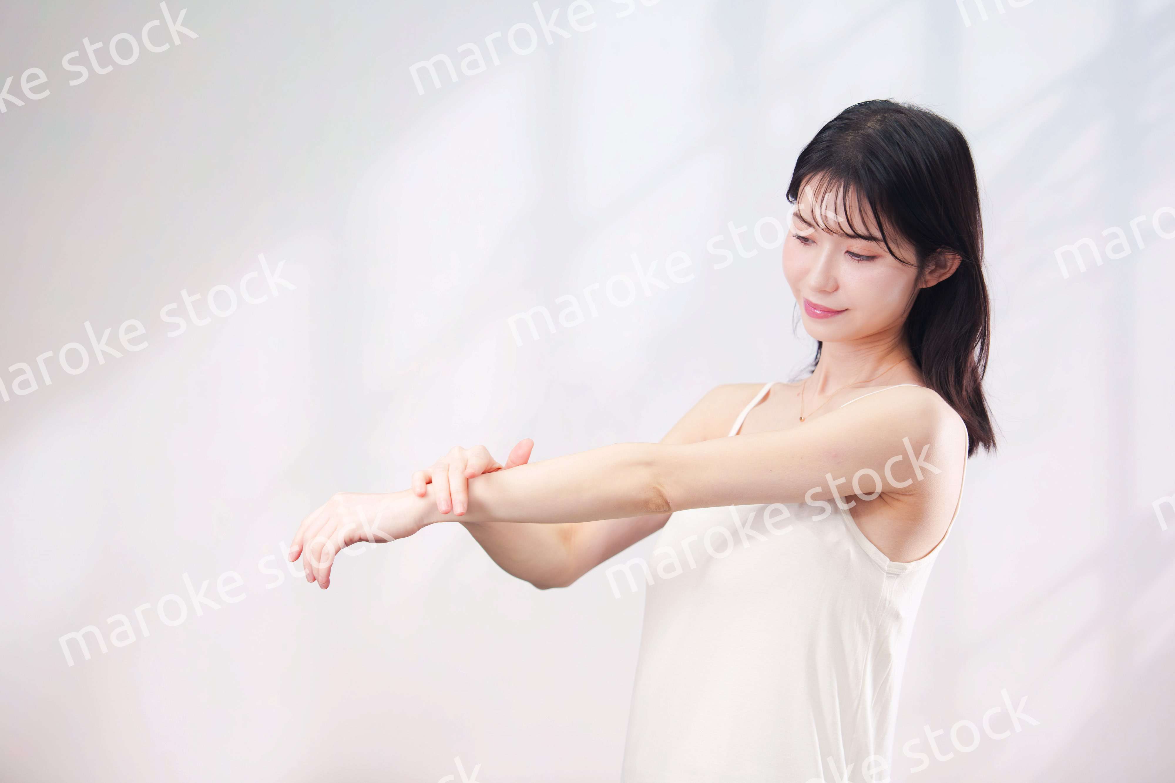 腕にクリームを塗る若い女性（シンプル背景）