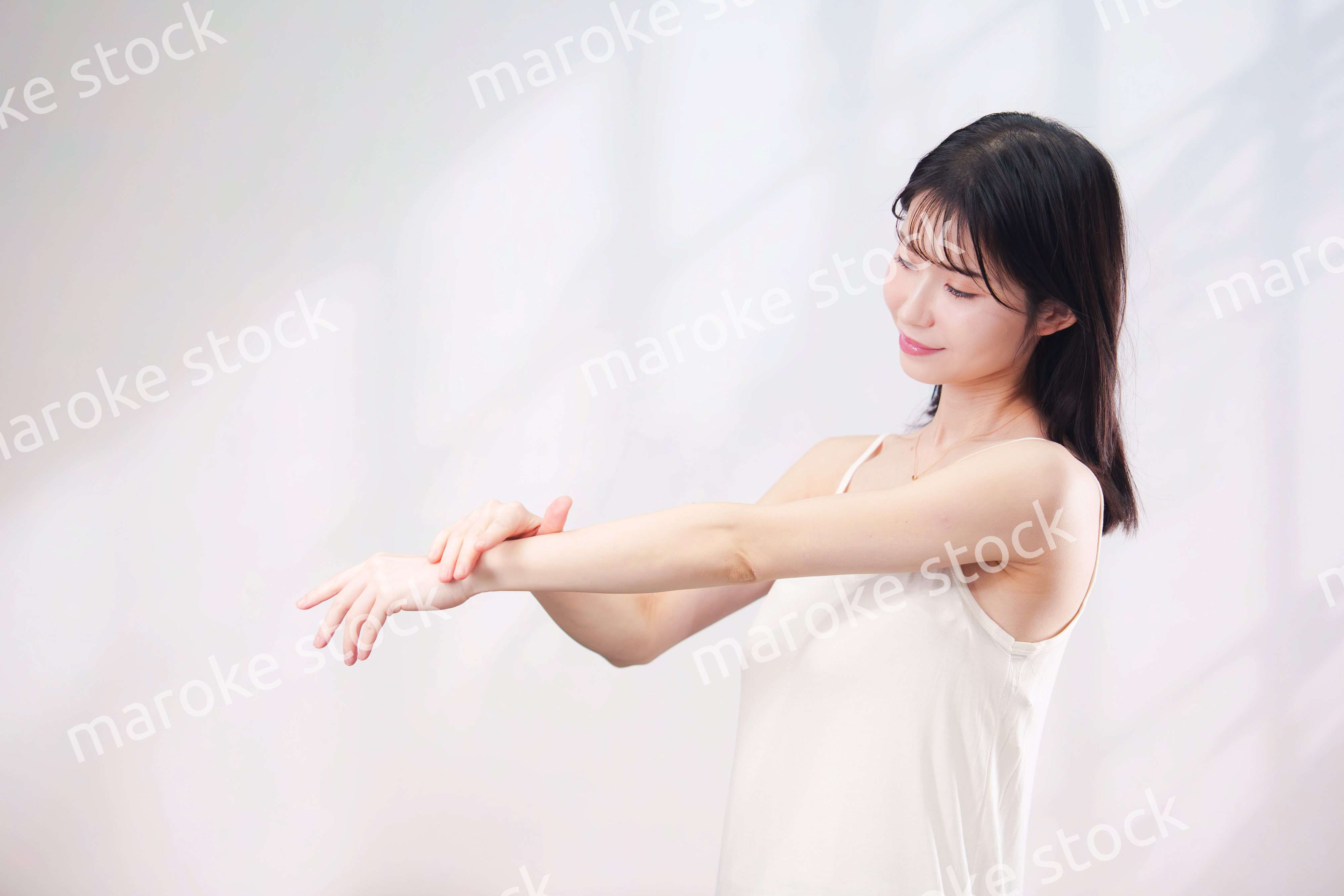 腕にクリームを塗る若い女性（シンプル背景）