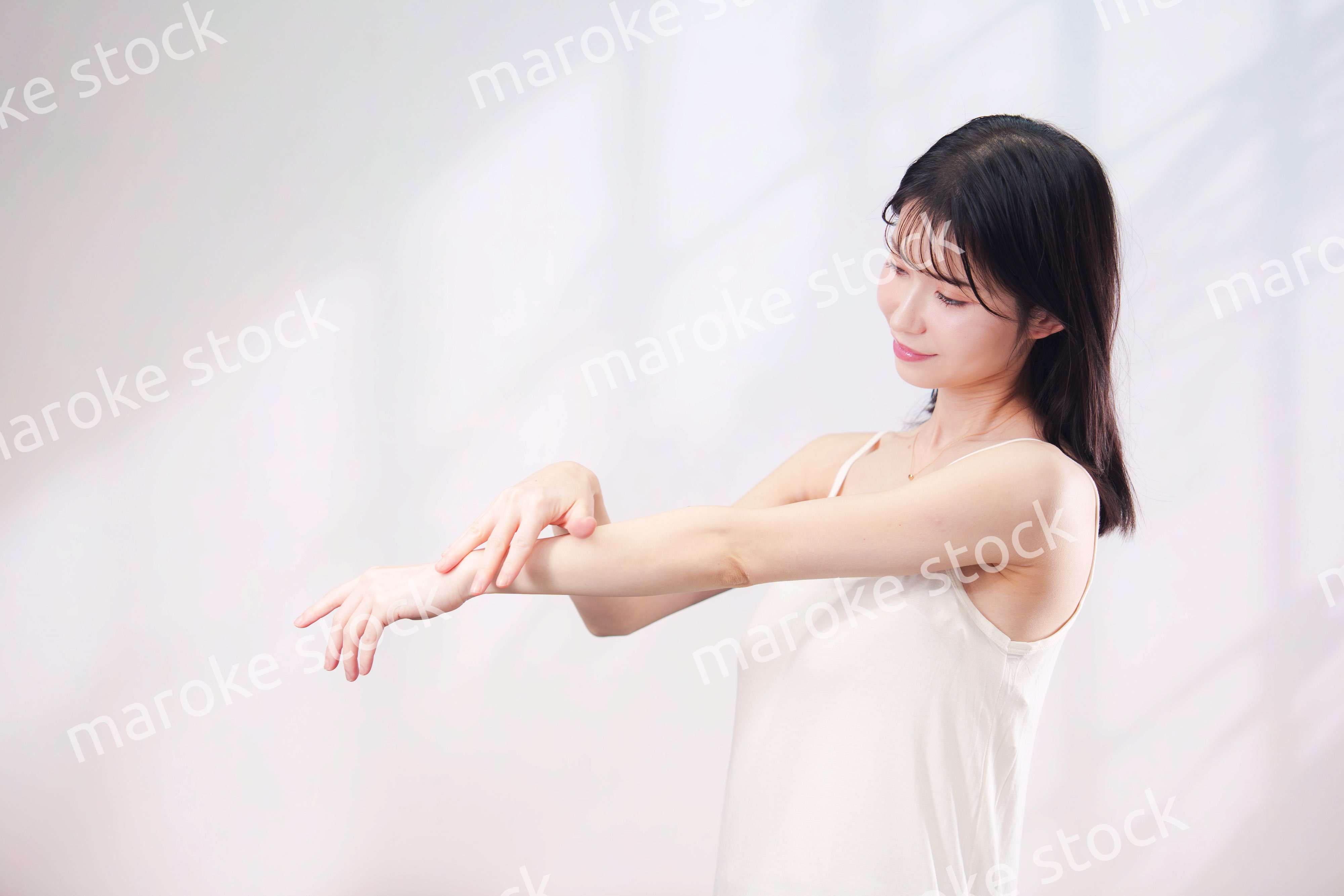 腕にクリームを塗る若い女性（シンプル背景）