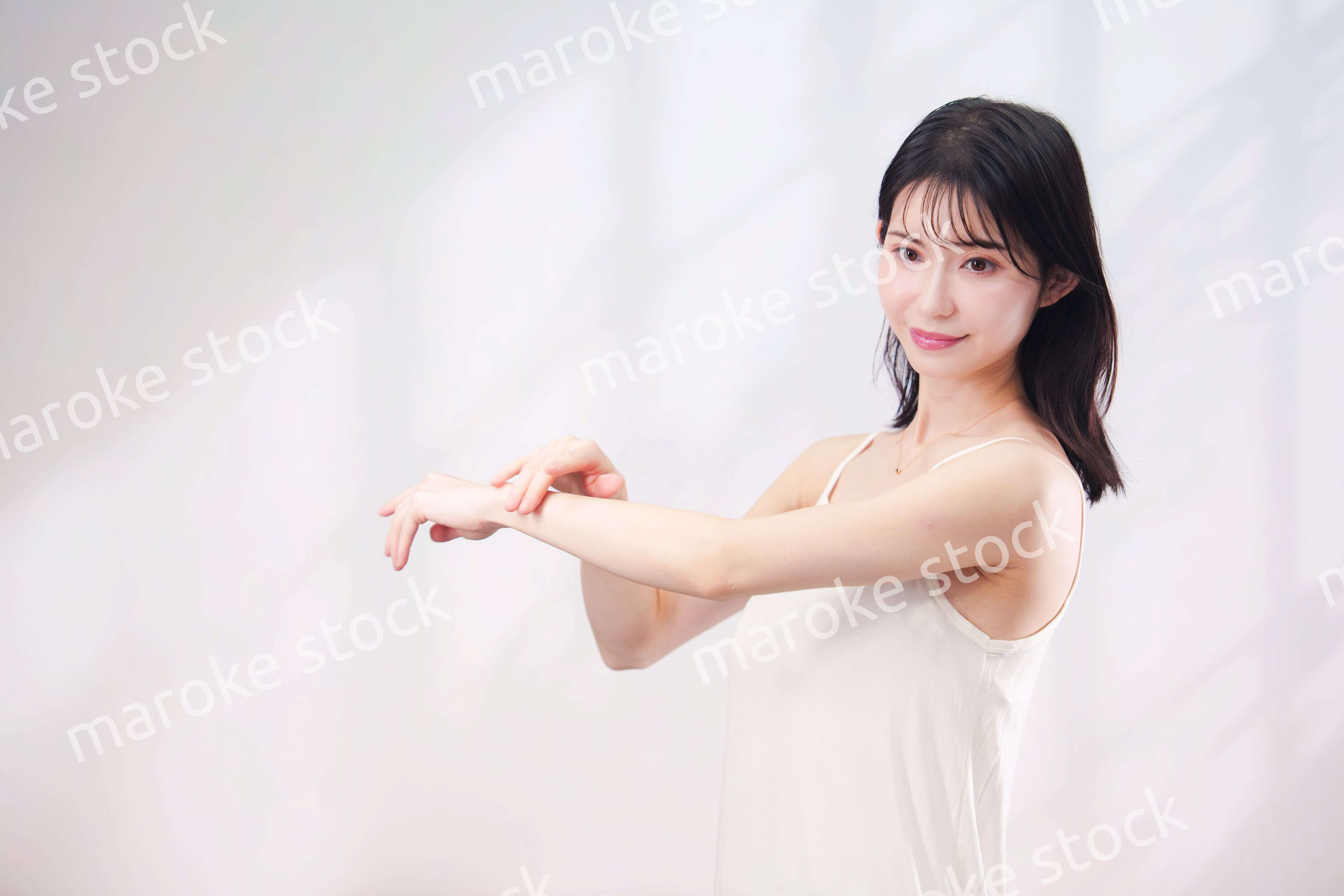 腕にクリームを塗る若い女性（シンプル背景）