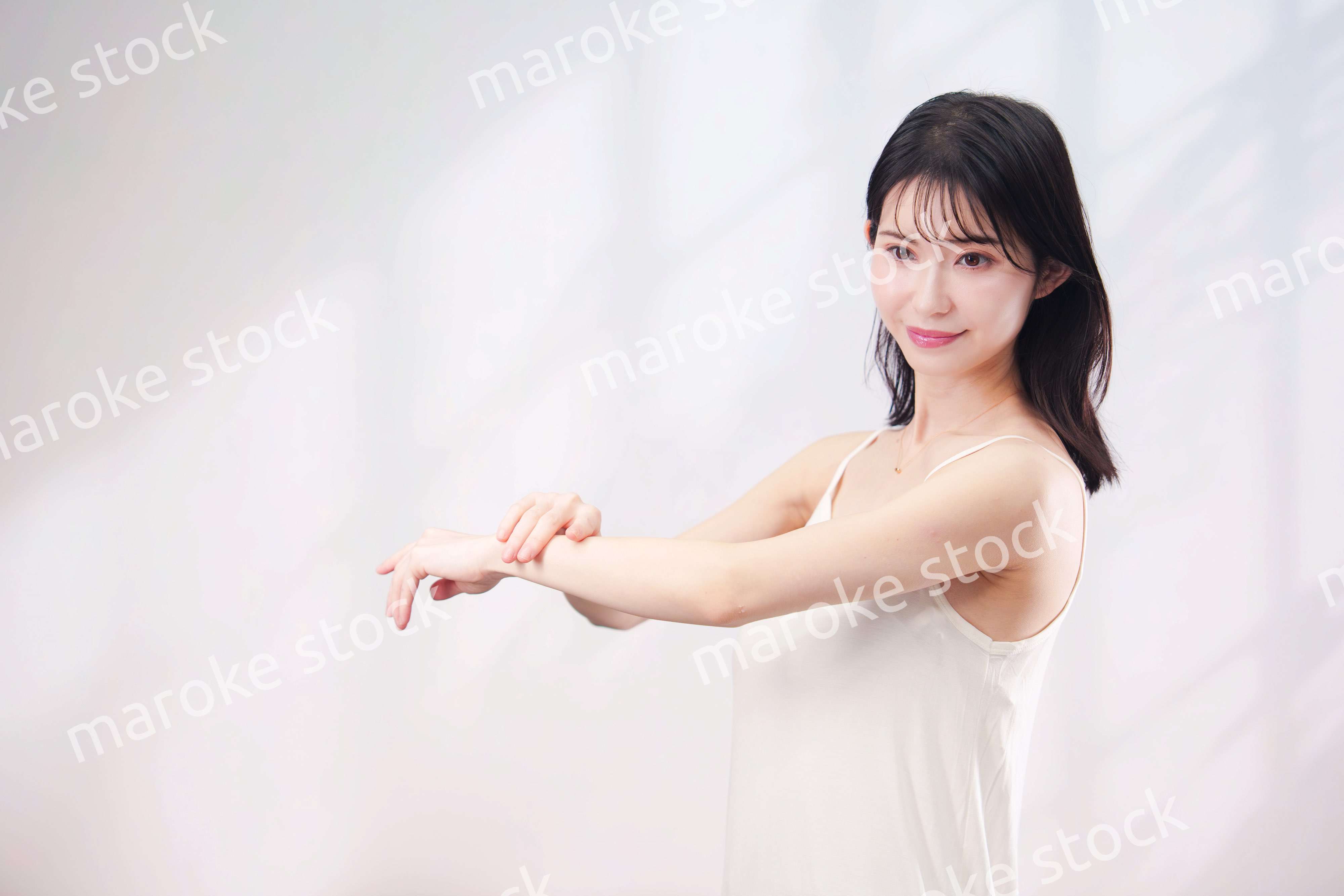 腕にクリームを塗る若い女性（シンプル背景）