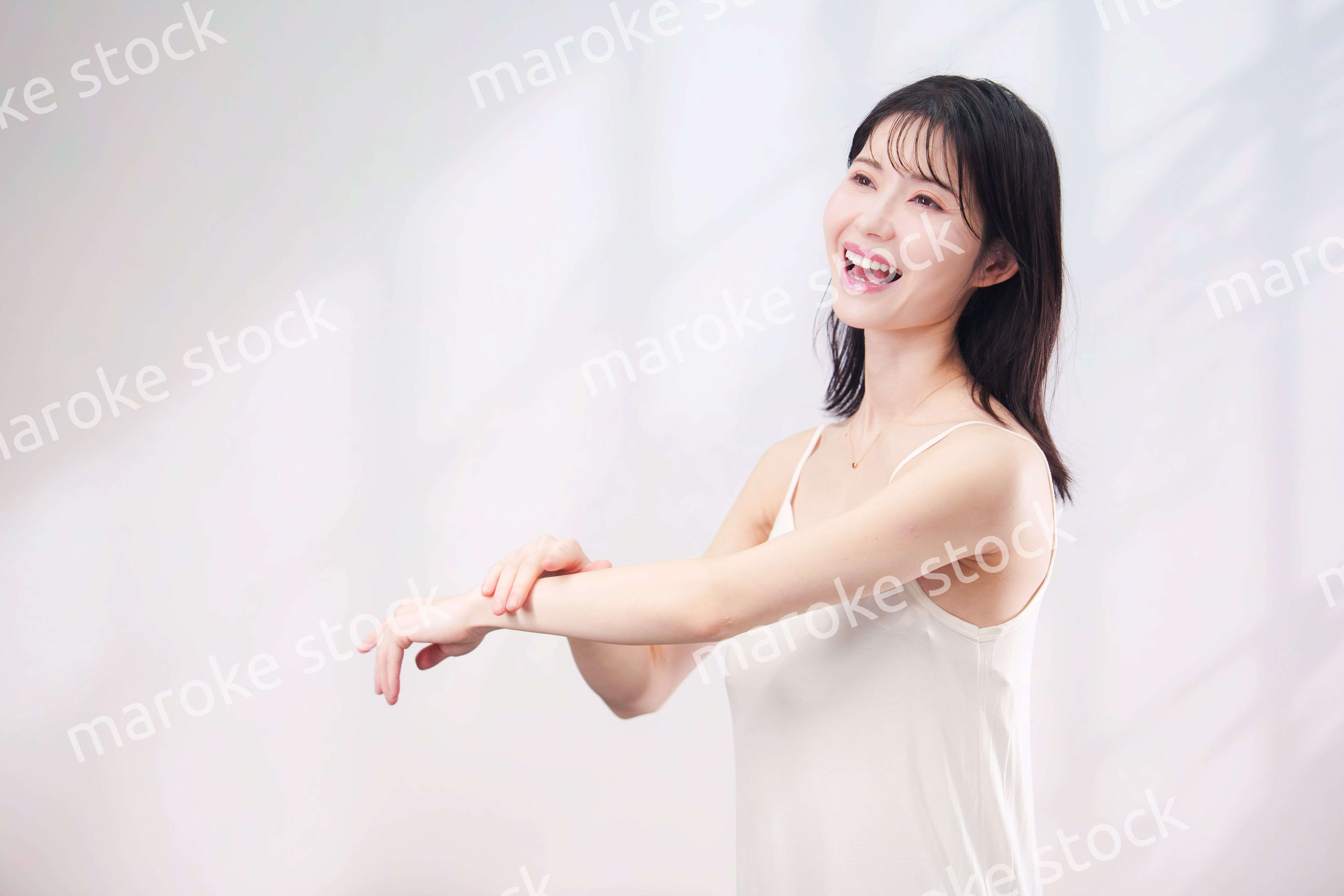 腕にクリームを塗る若い女性（シンプル背景）