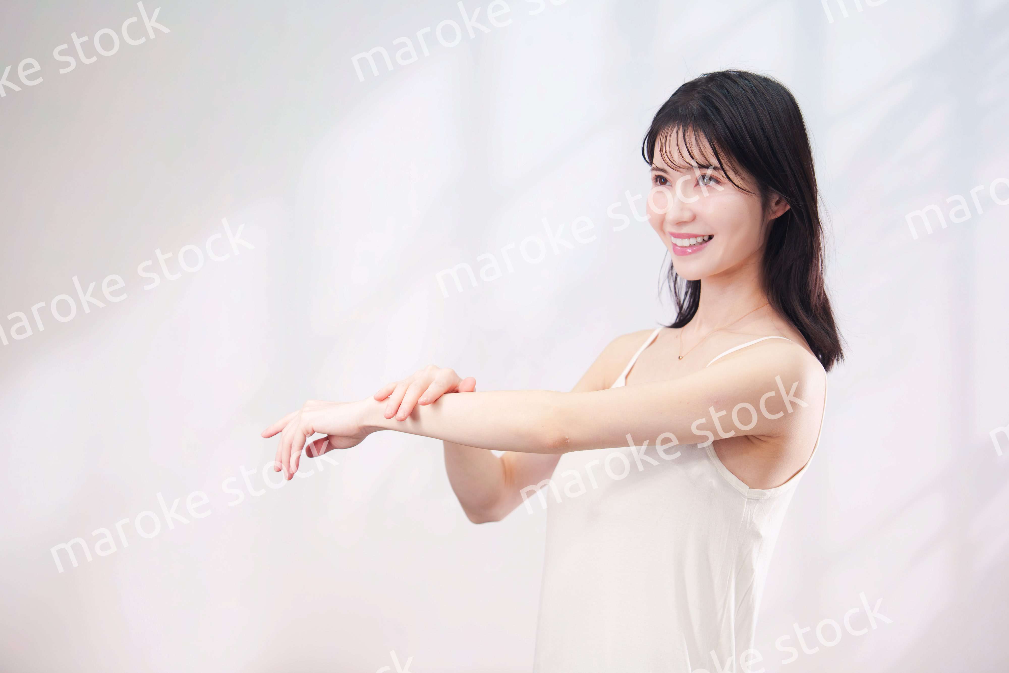 腕にクリームを塗る若い女性（シンプル背景）