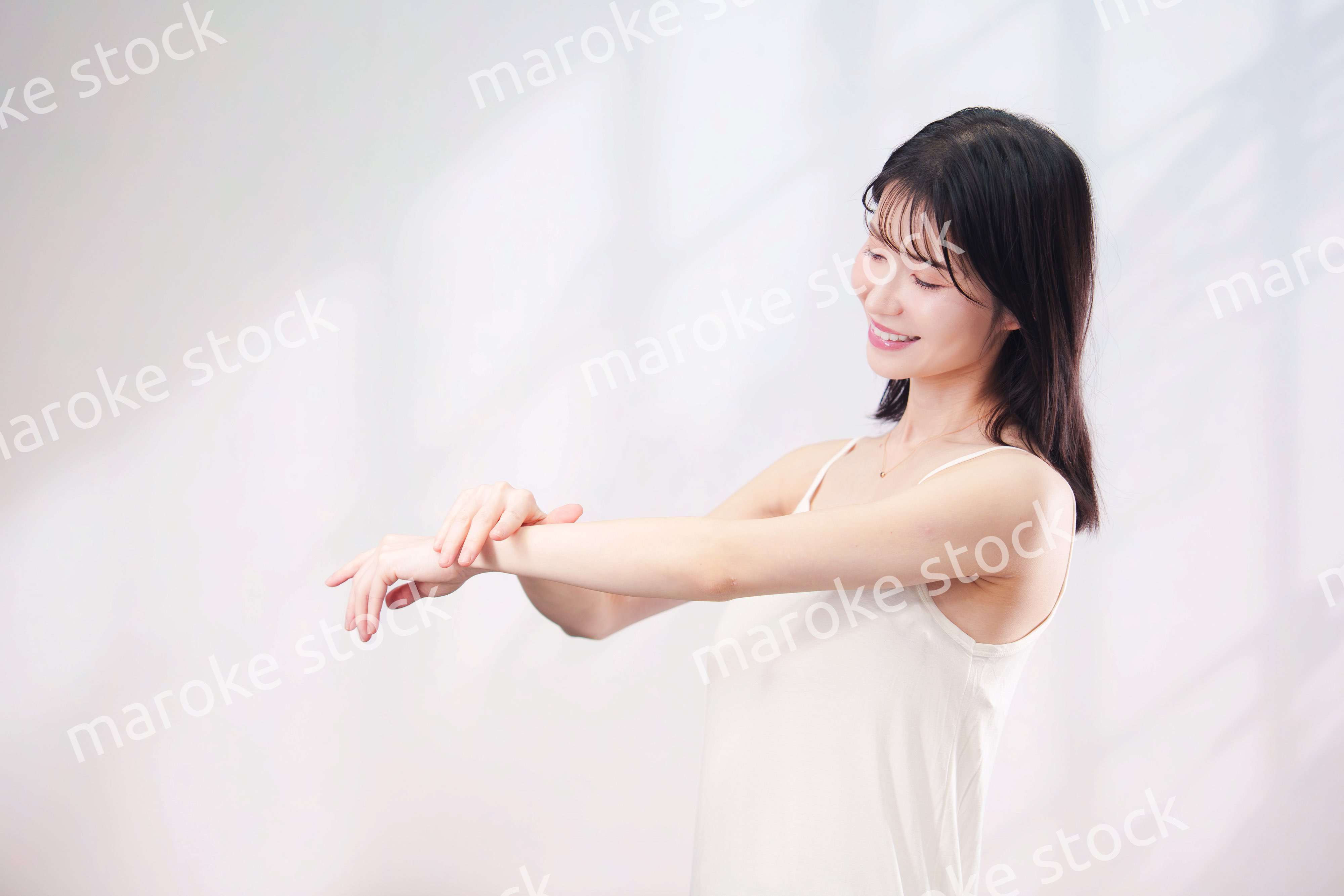 腕にクリームを塗る若い女性（シンプル背景）