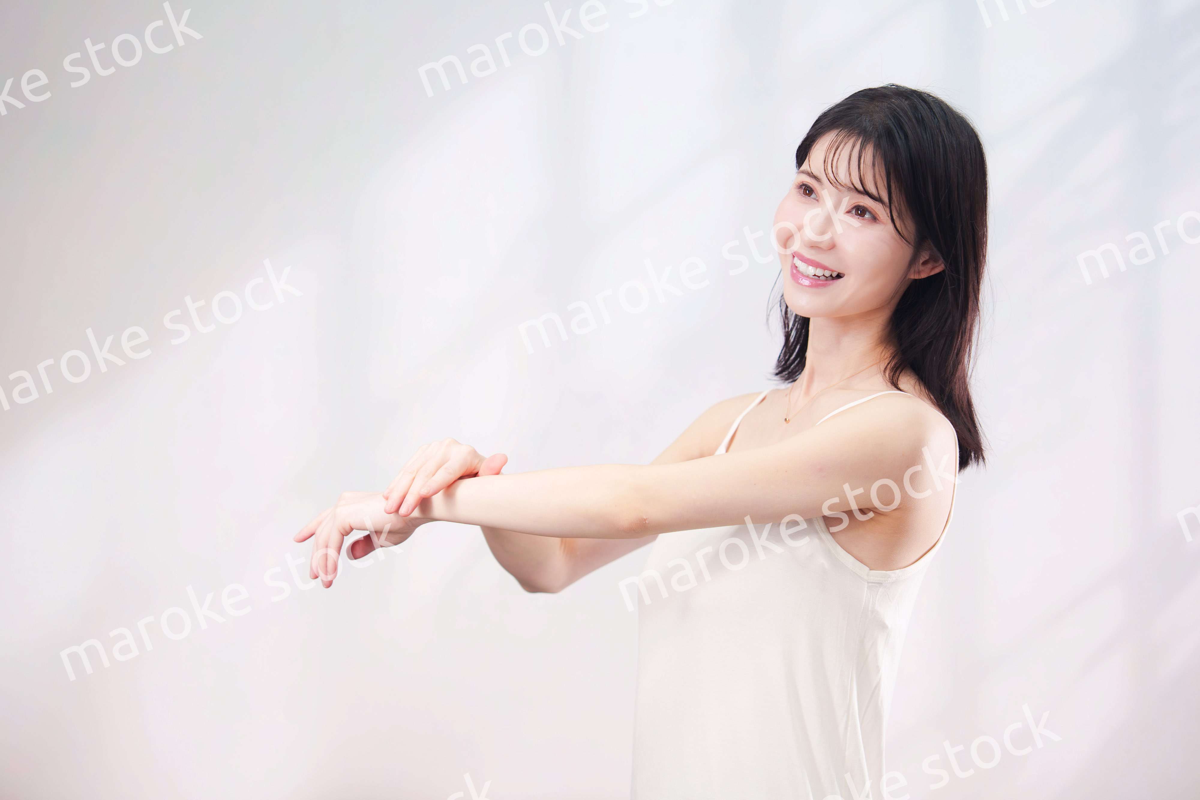 腕にクリームを塗る若い女性（シンプル背景）