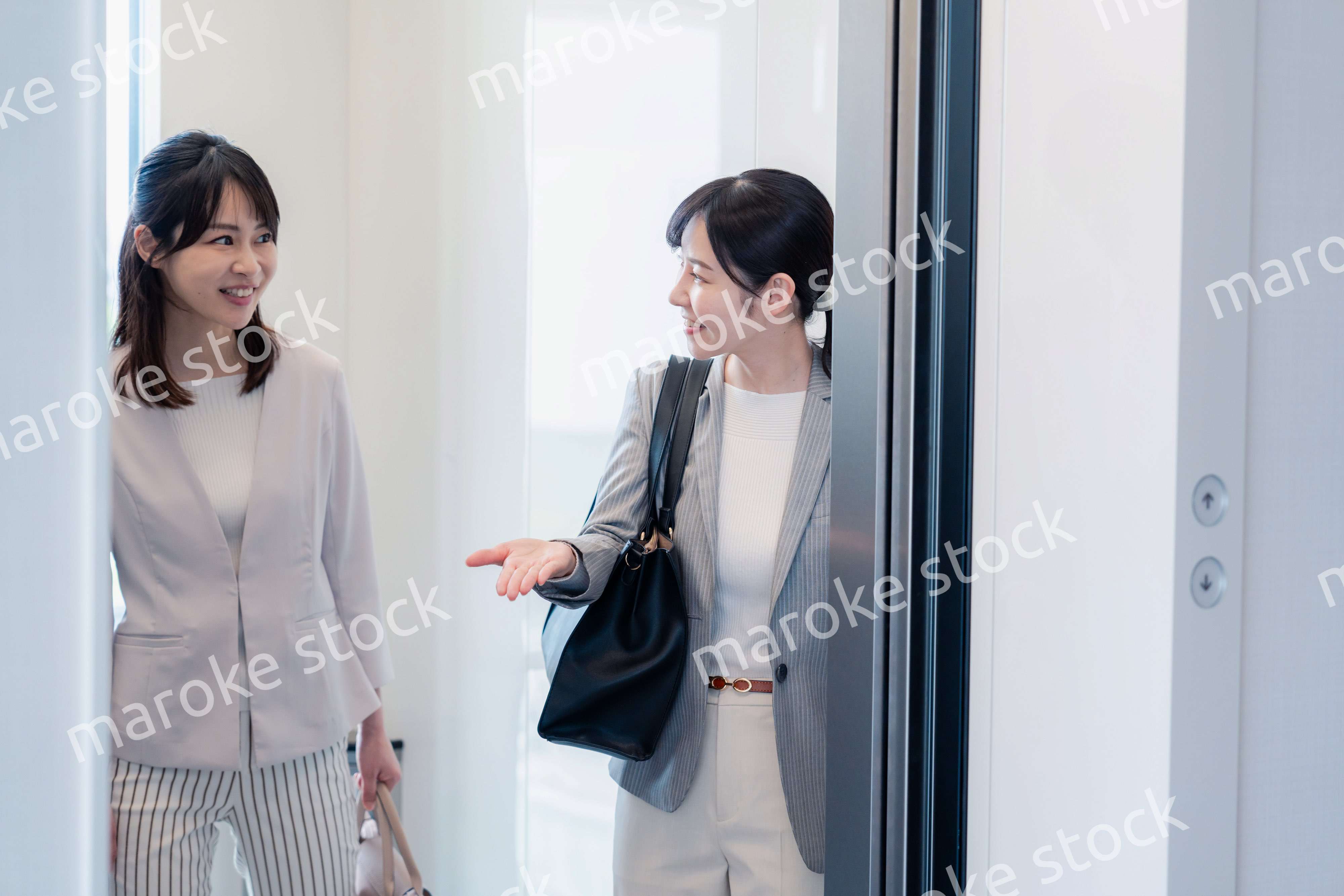 エレベーターで譲り合う2人のビジネスパーソン