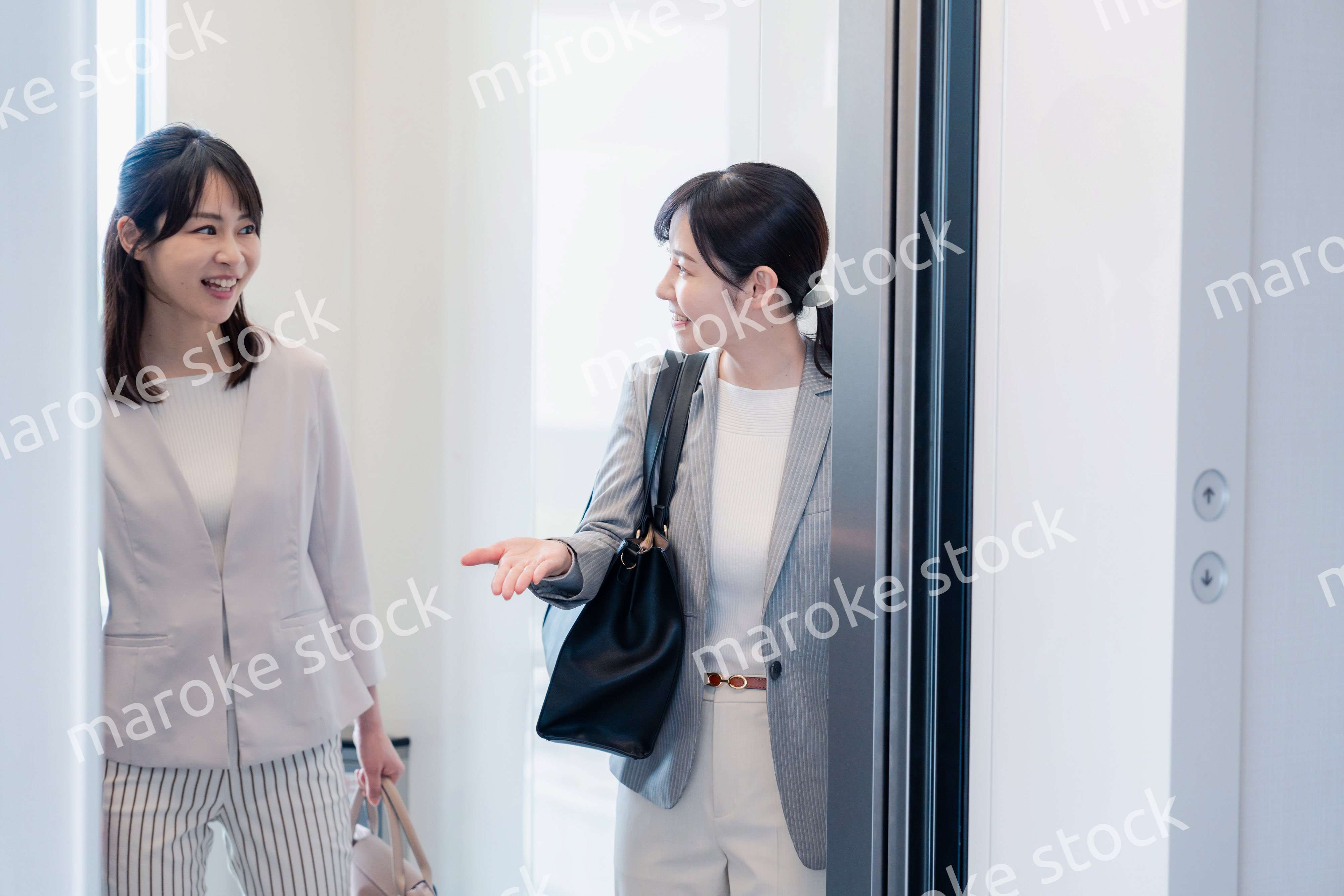 エレベーターで譲り合う2人のビジネスパーソン