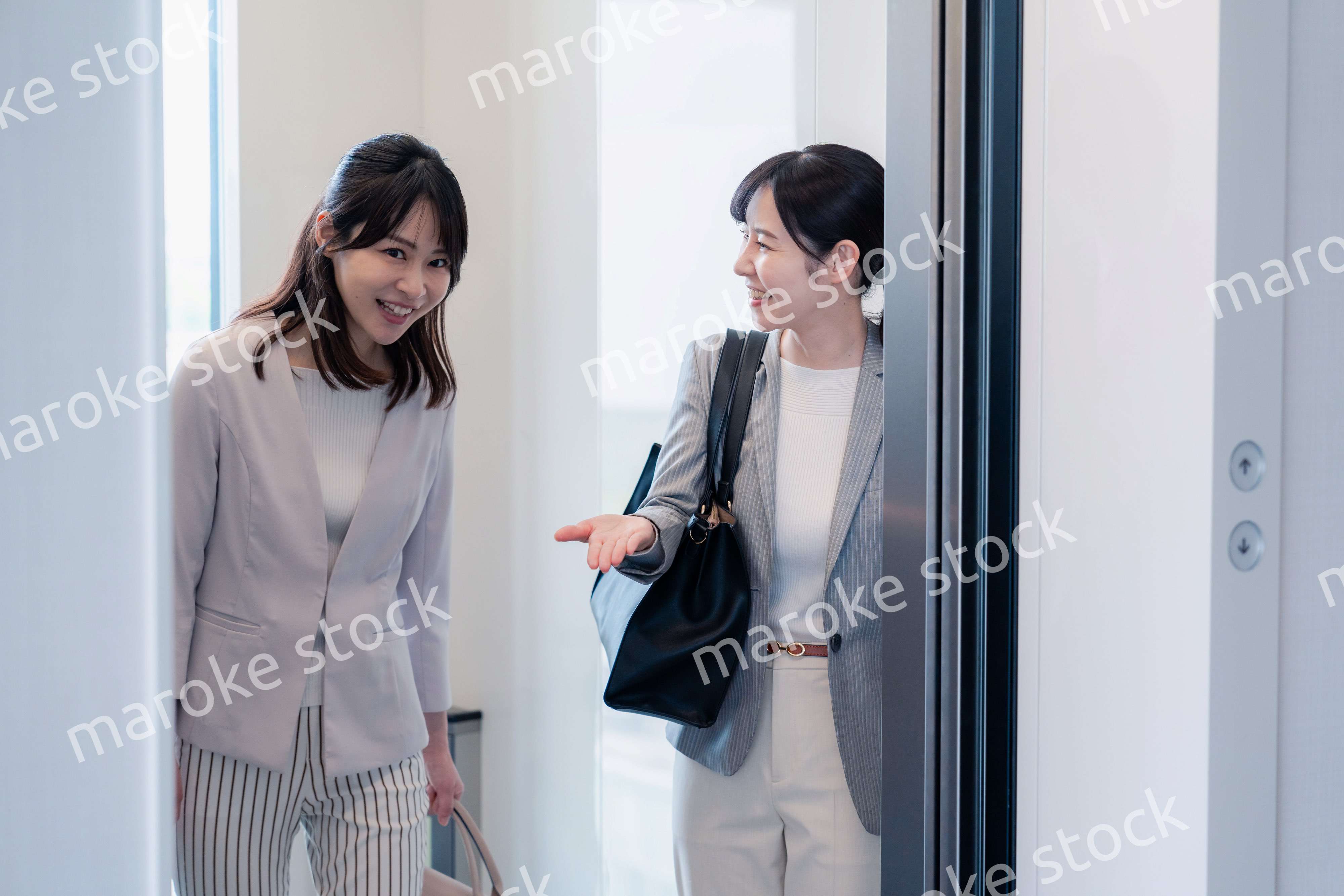 エレベーターで譲り合う2人のビジネスパーソン