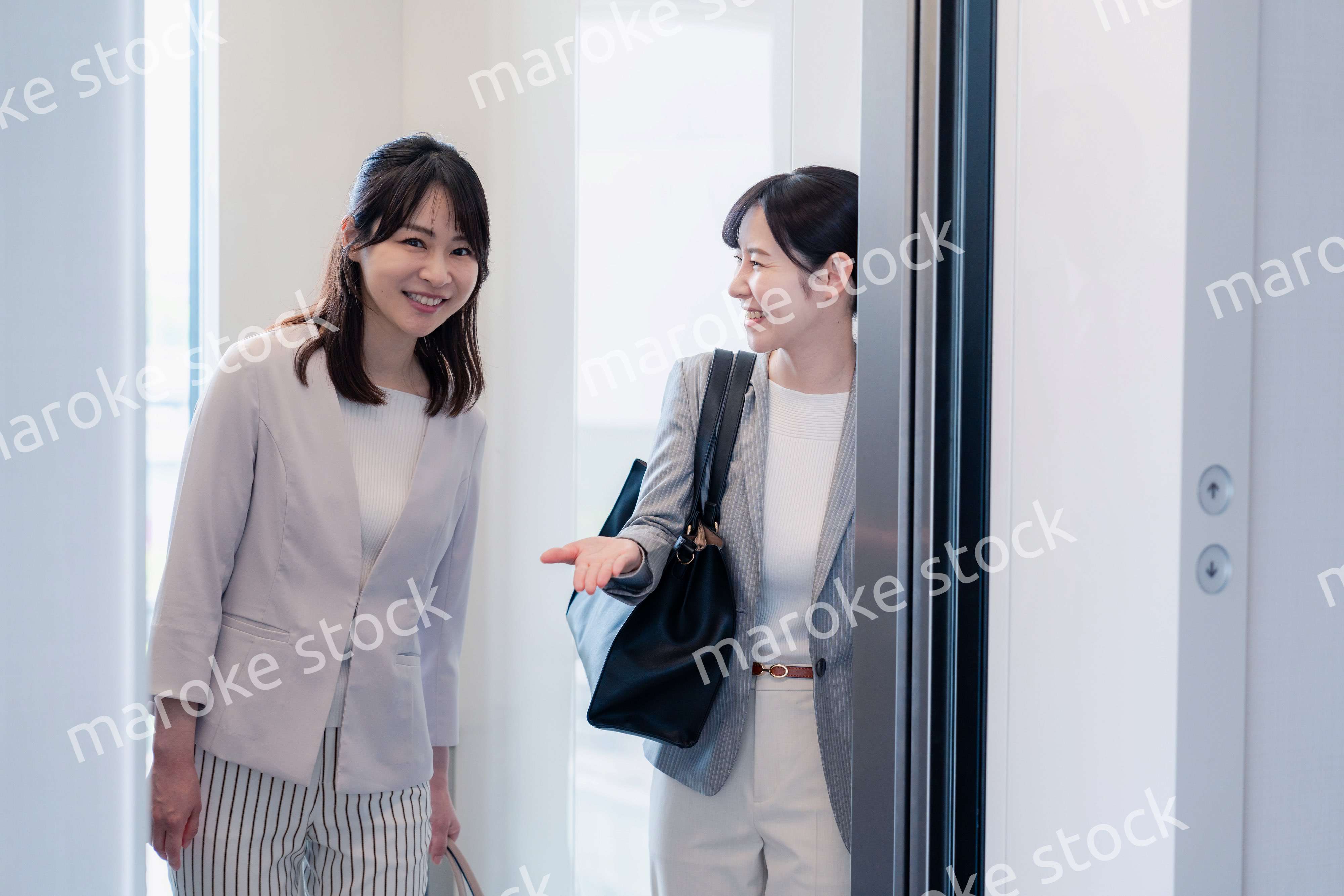 エレベーターで譲り合う2人のビジネスパーソン