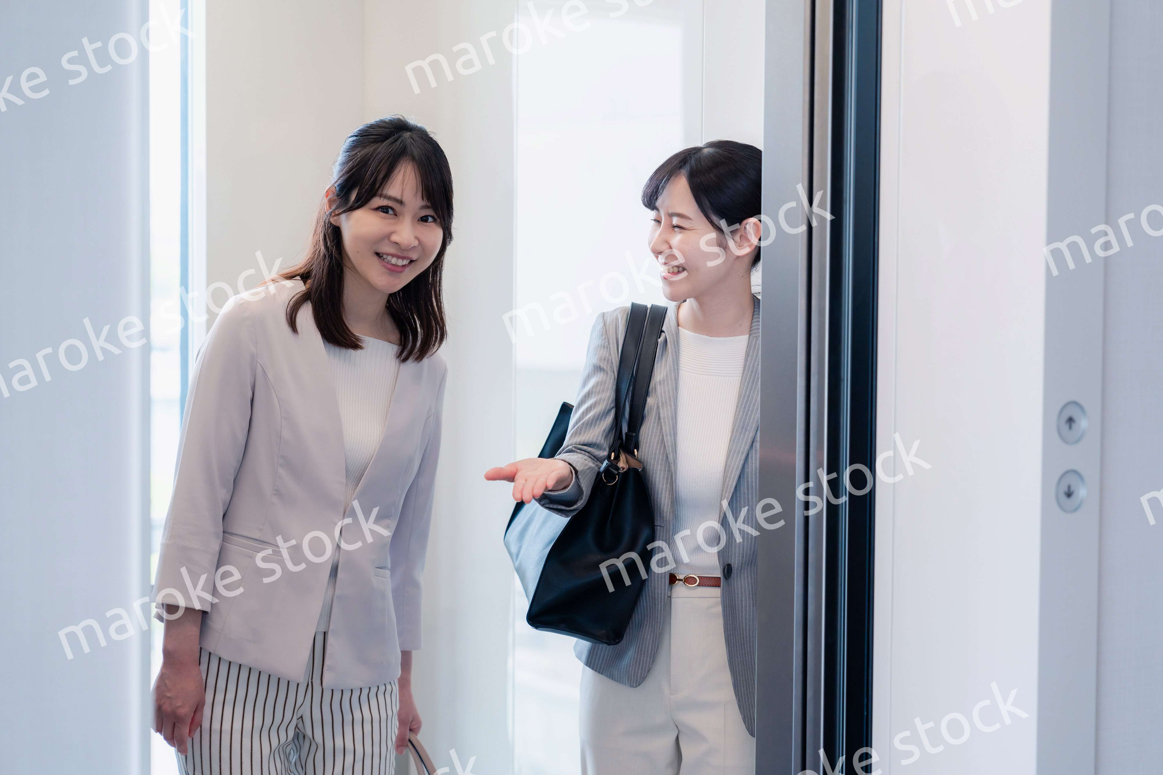 エレベーターで譲り合う2人のビジネスパーソン