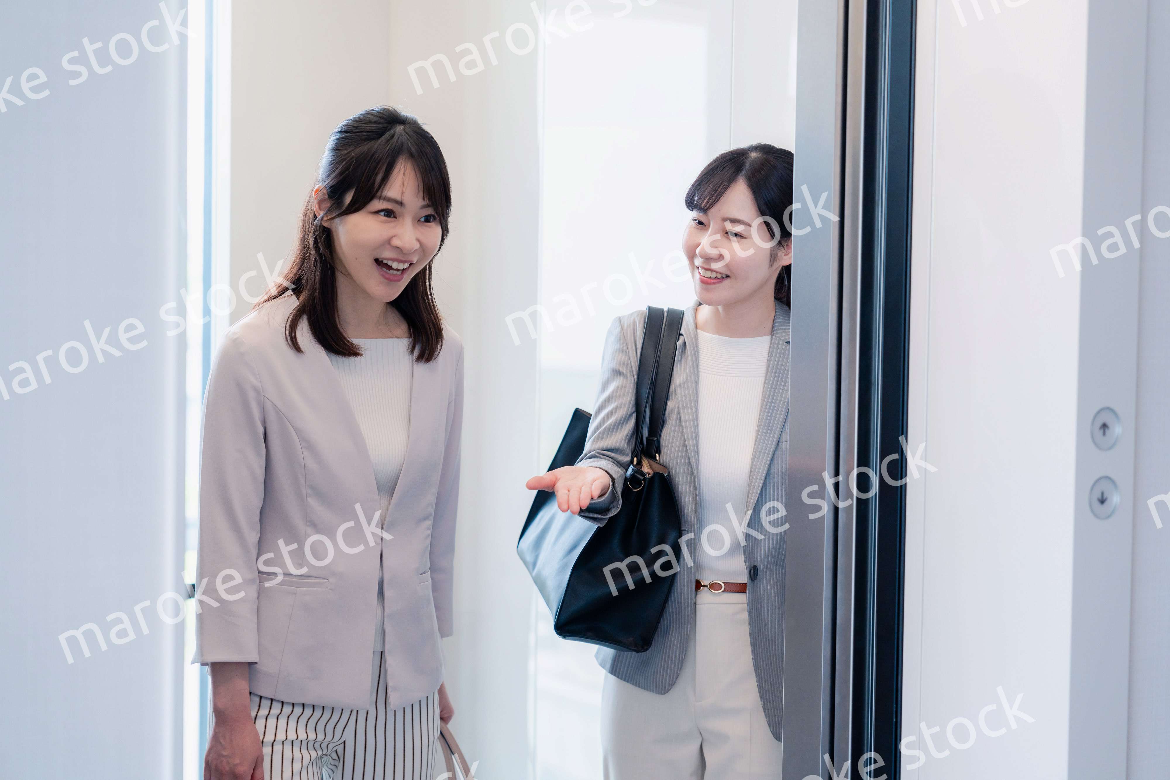 エレベーターで譲り合う2人のビジネスパーソン