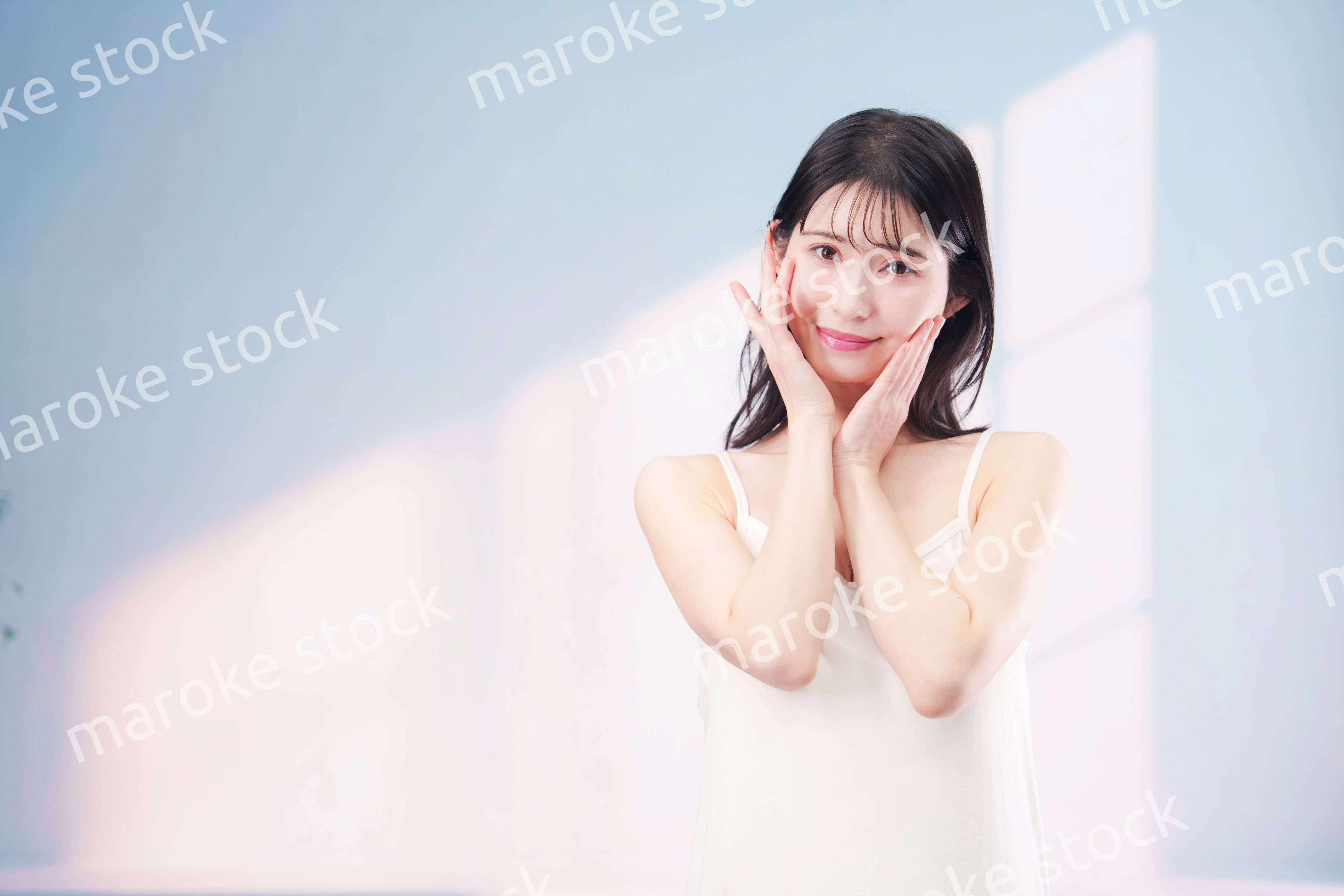 笑顔でお肌のケアをする若い女性（シンプル背景）