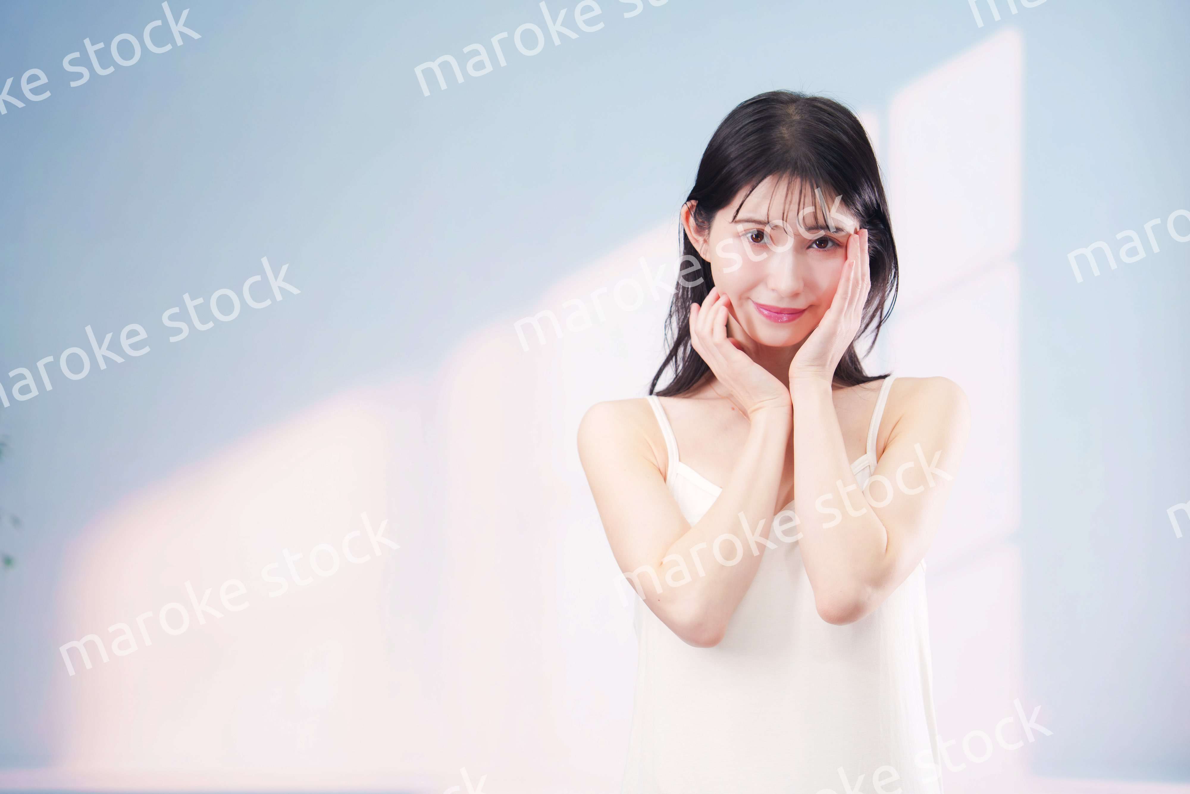 笑顔でお肌のケアをする若い女性（シンプル背景）