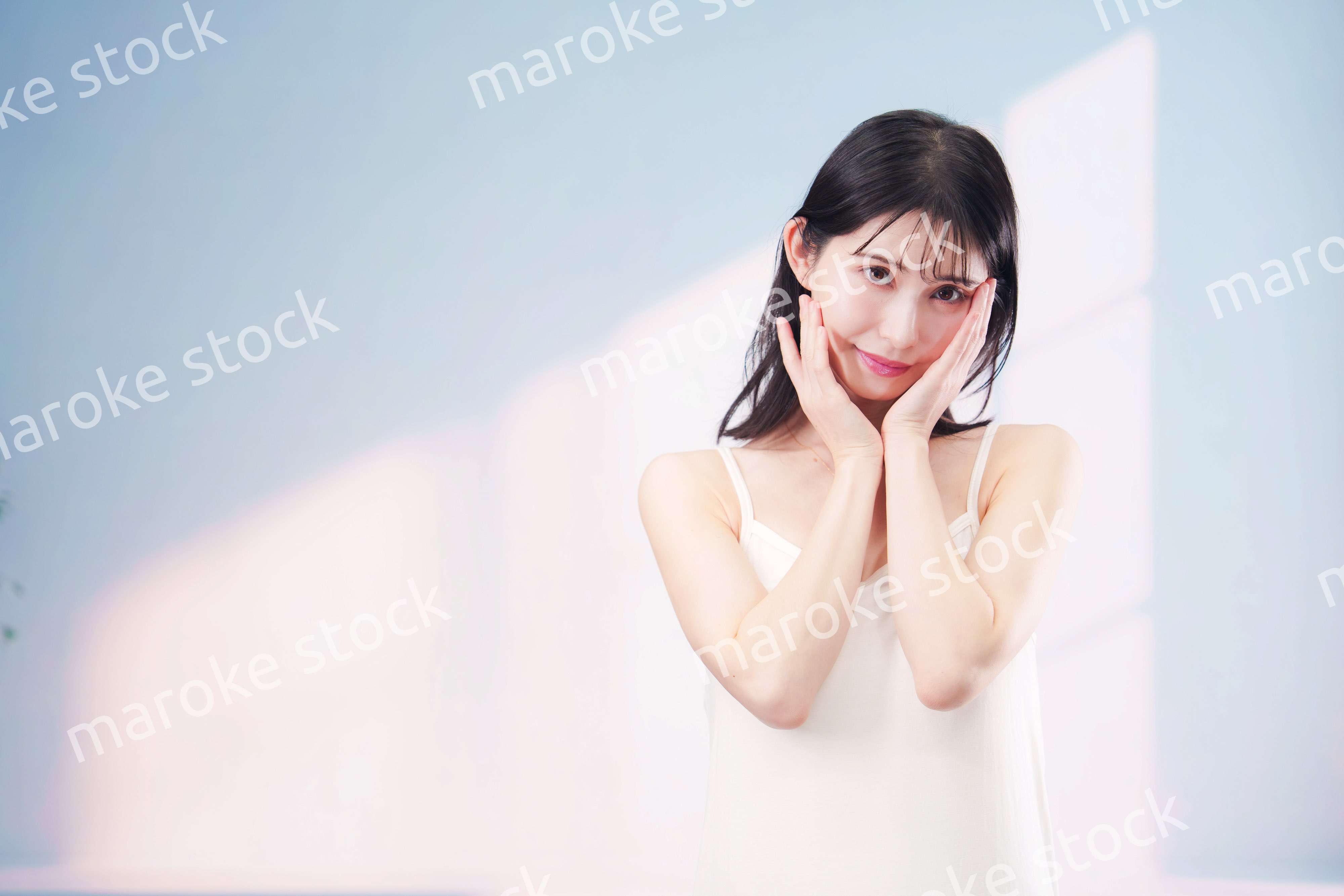 笑顔でお肌のケアをする若い女性（シンプル背景）