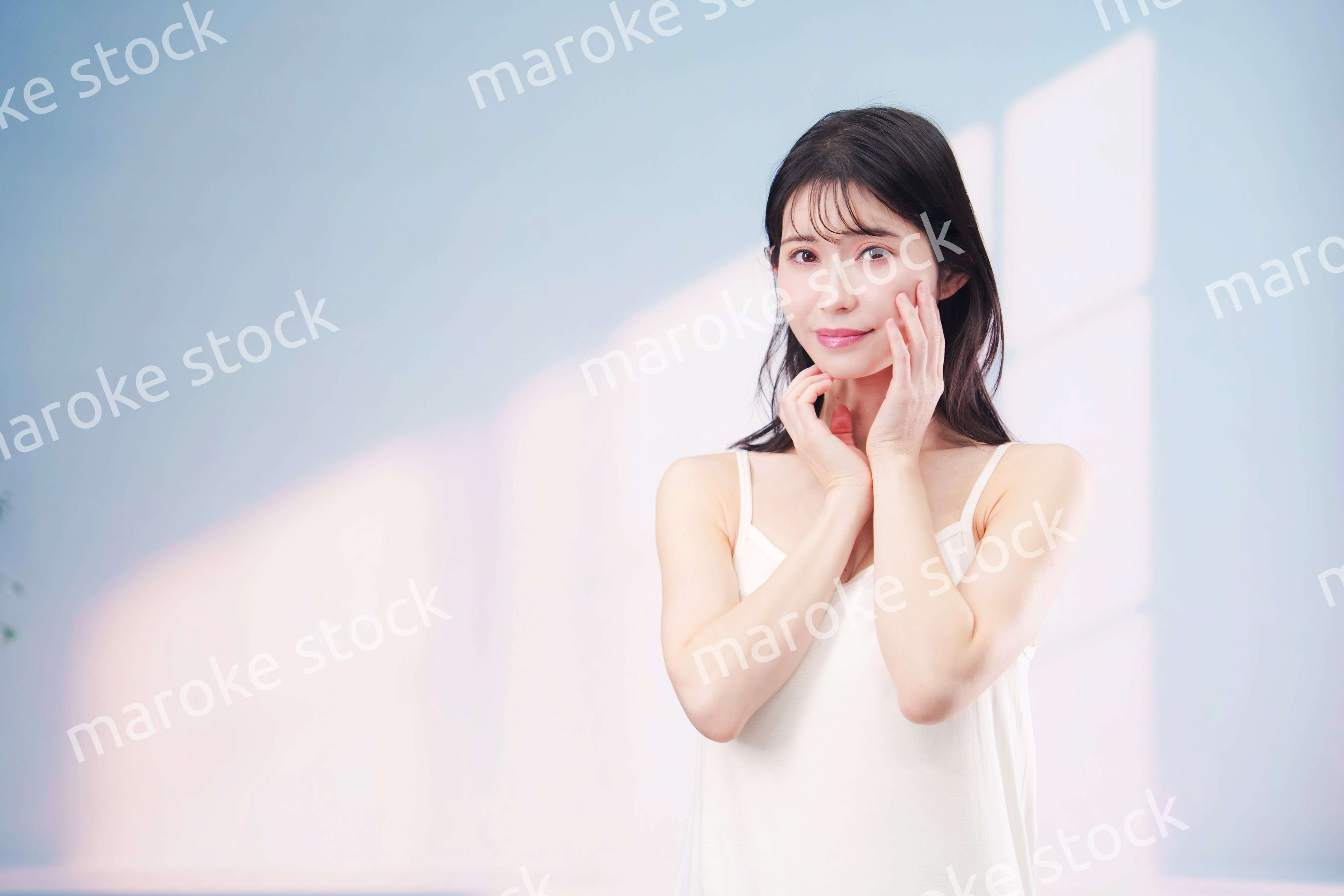 笑顔でお肌のケアをする若い女性（シンプル背景）