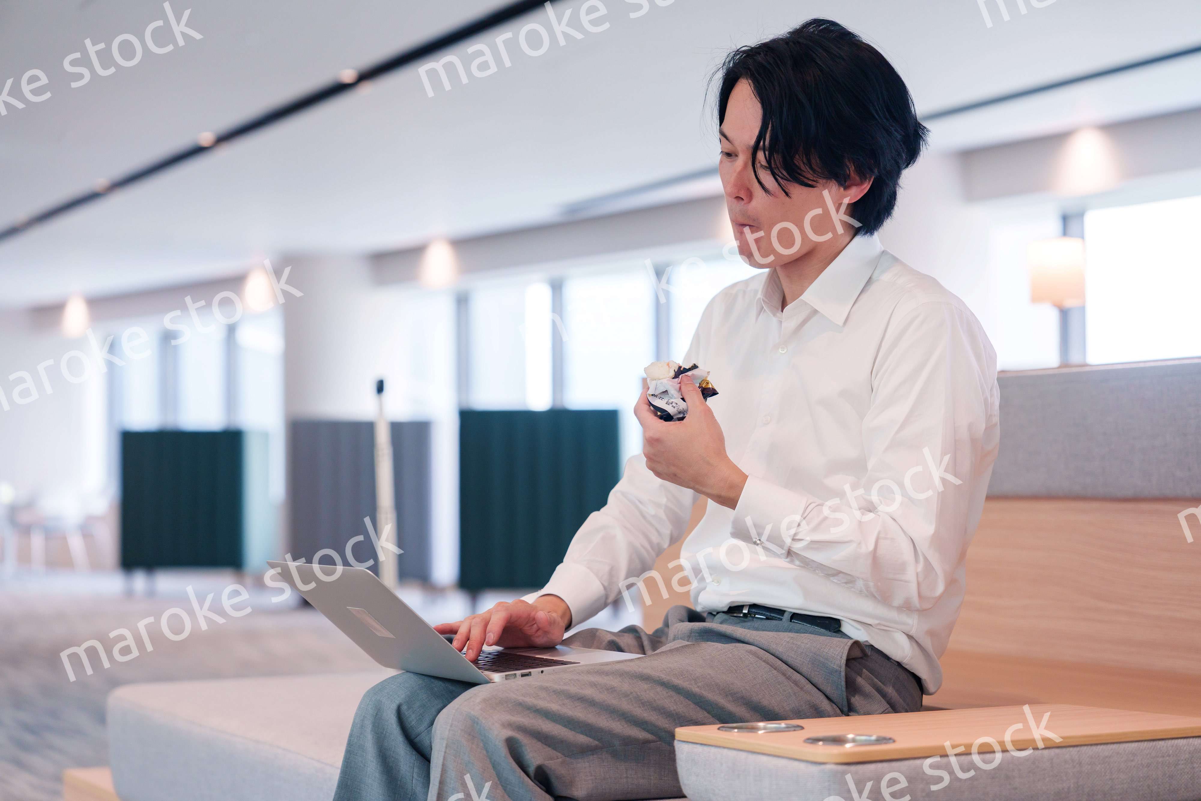 お昼ごはんを食べながらオフィスで仕事をする男性