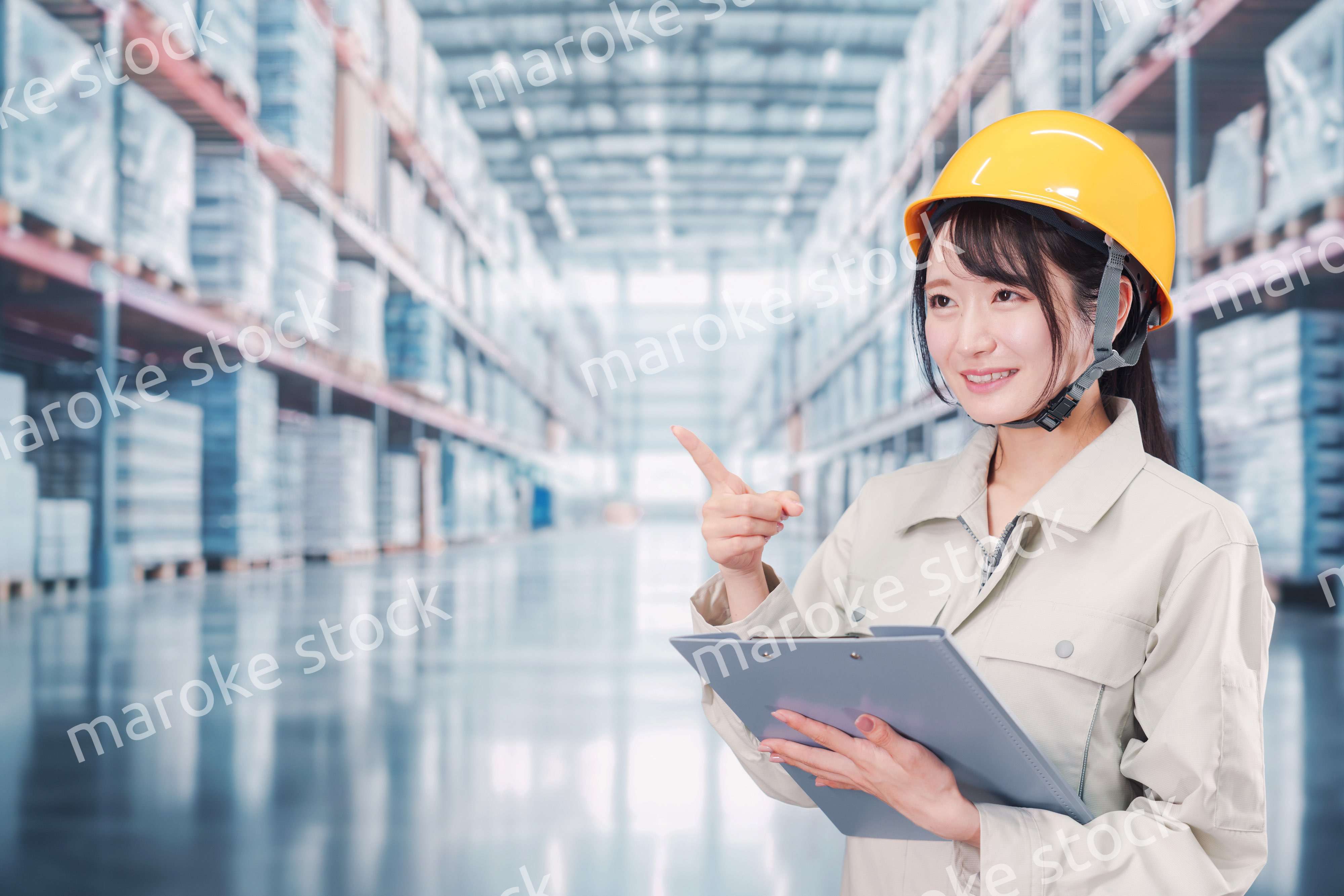 大きな物流倉庫で働くヘルメットを被った若い女性