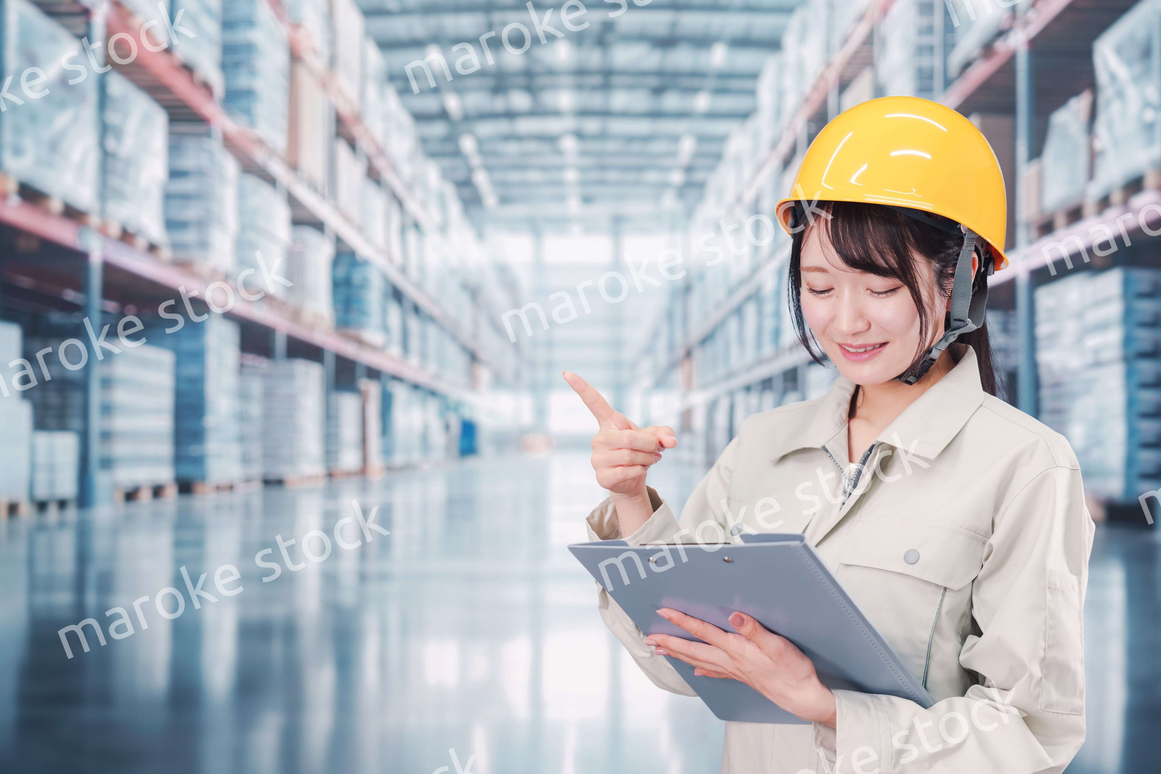 大きな物流倉庫で働くヘルメットを被った若い女性