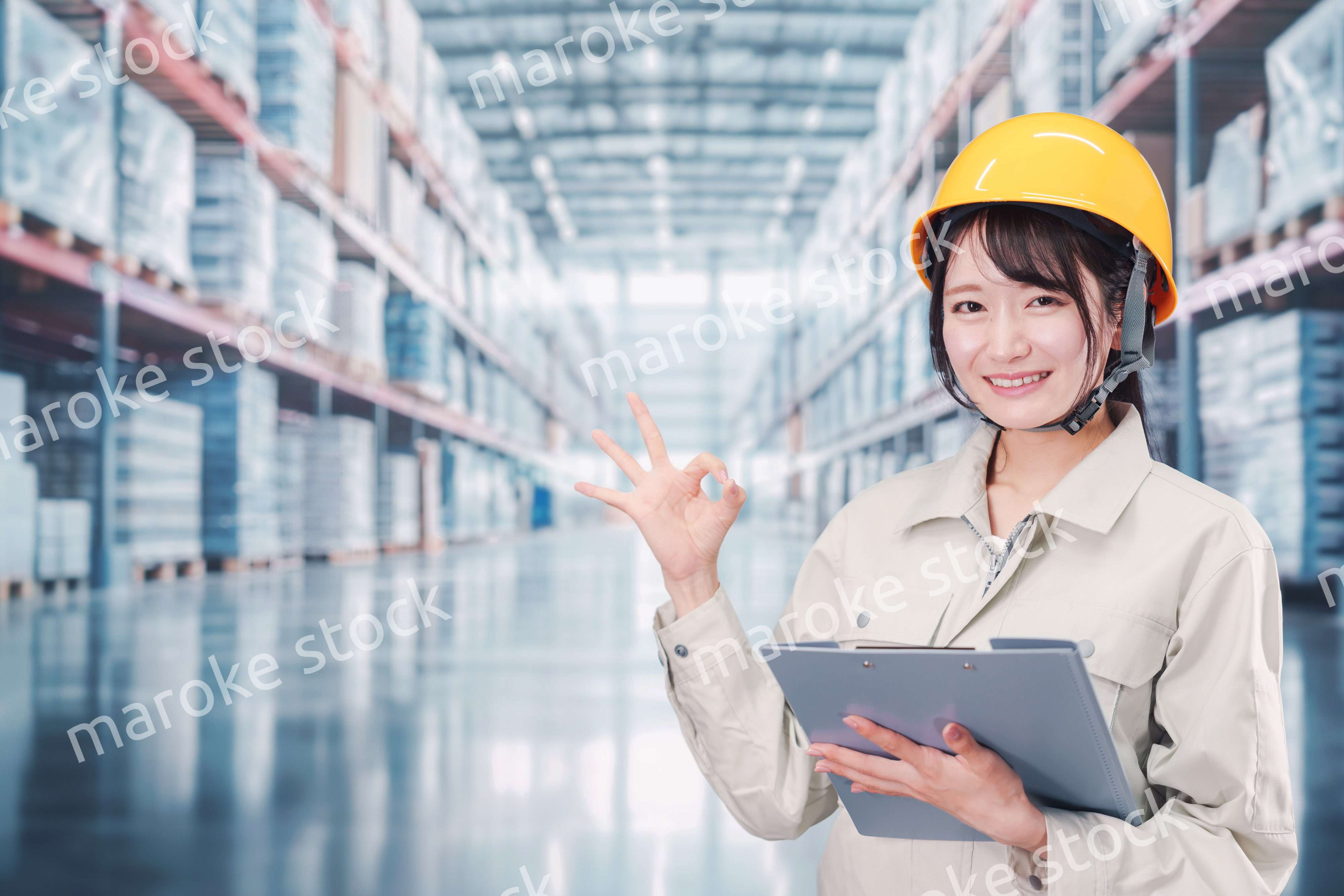 大きな物流倉庫で働くヘルメットを被った若い女性