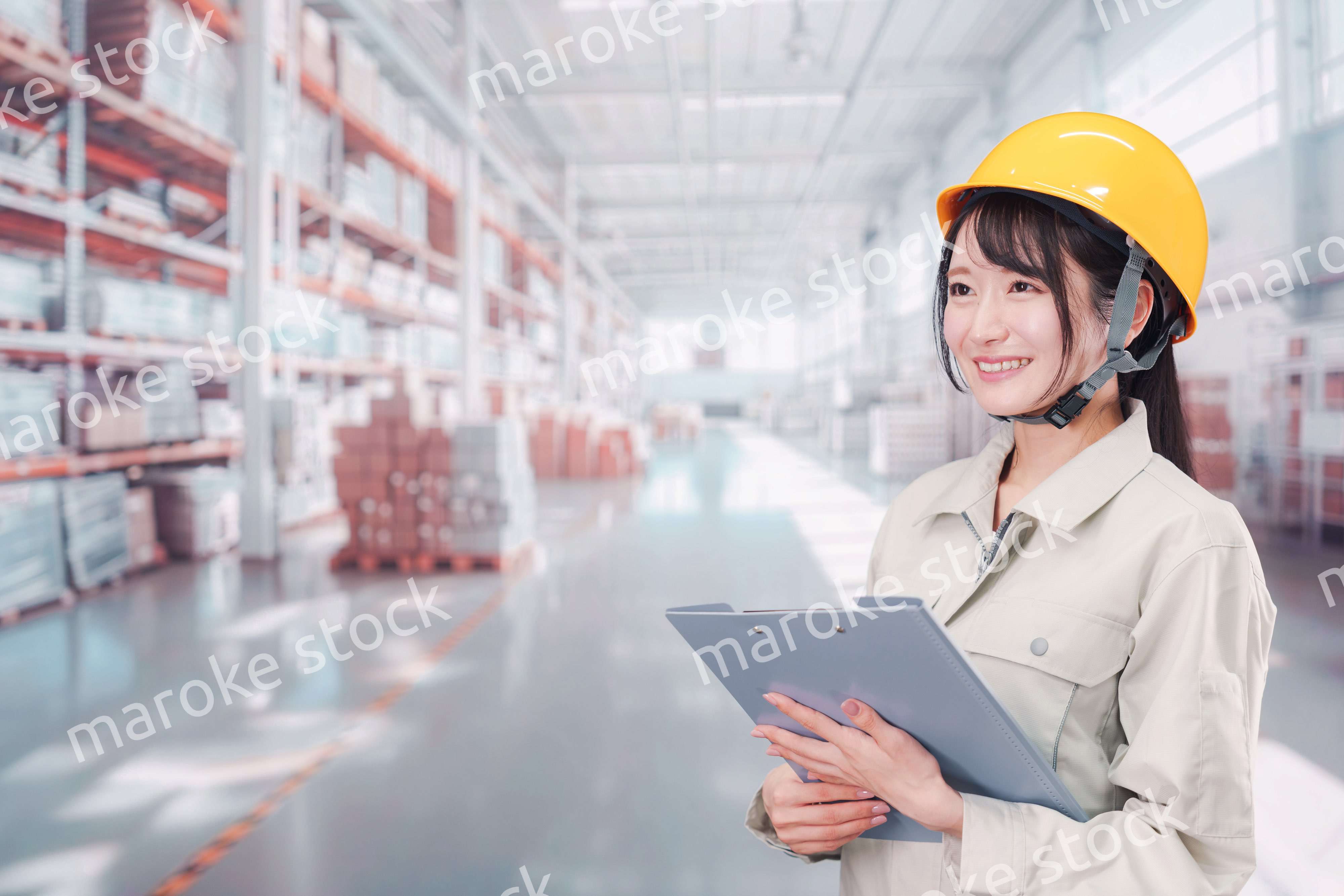 大きな物流倉庫で働くヘルメットを被った若い女性