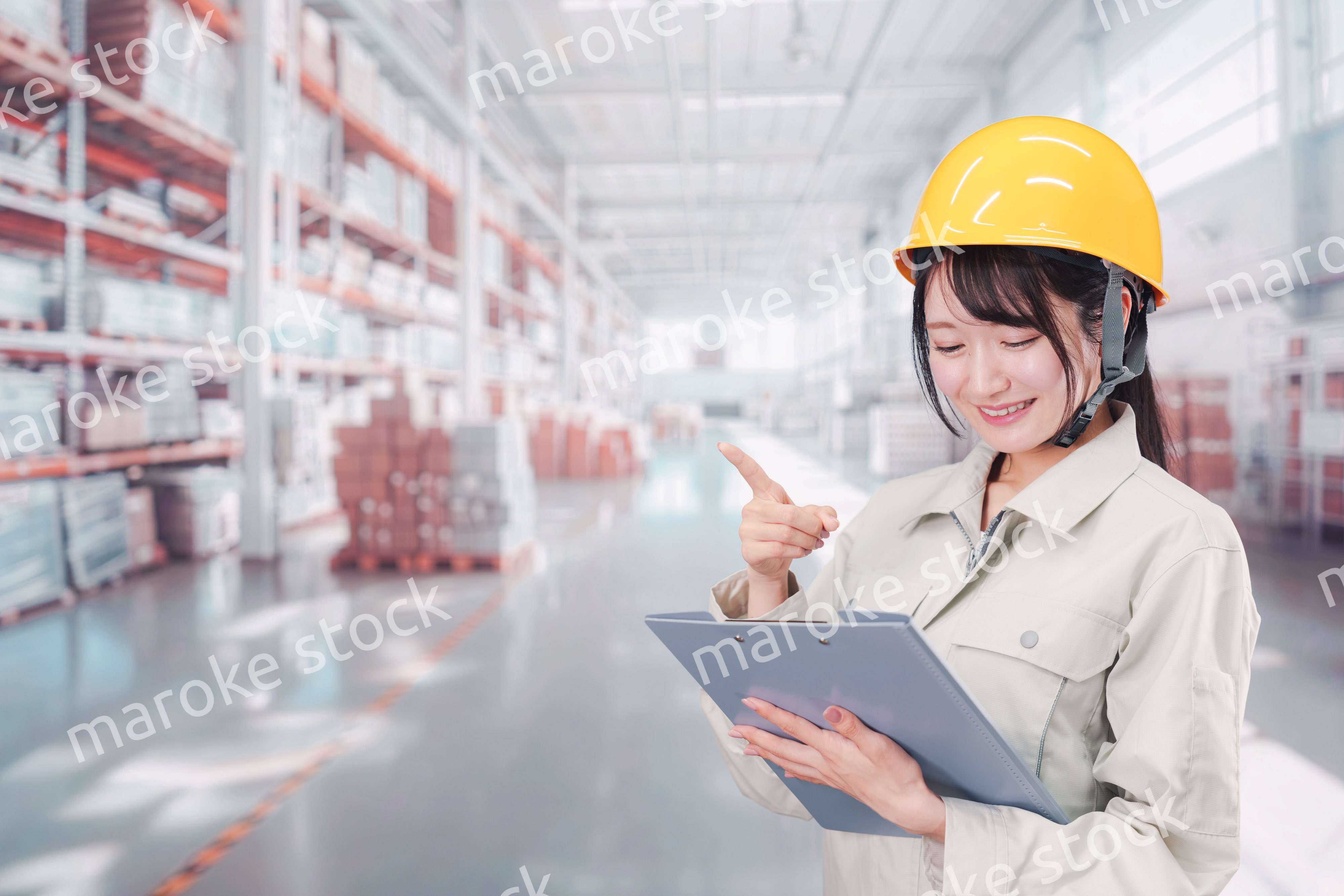 大きな物流倉庫で働くヘルメットを被った若い女性