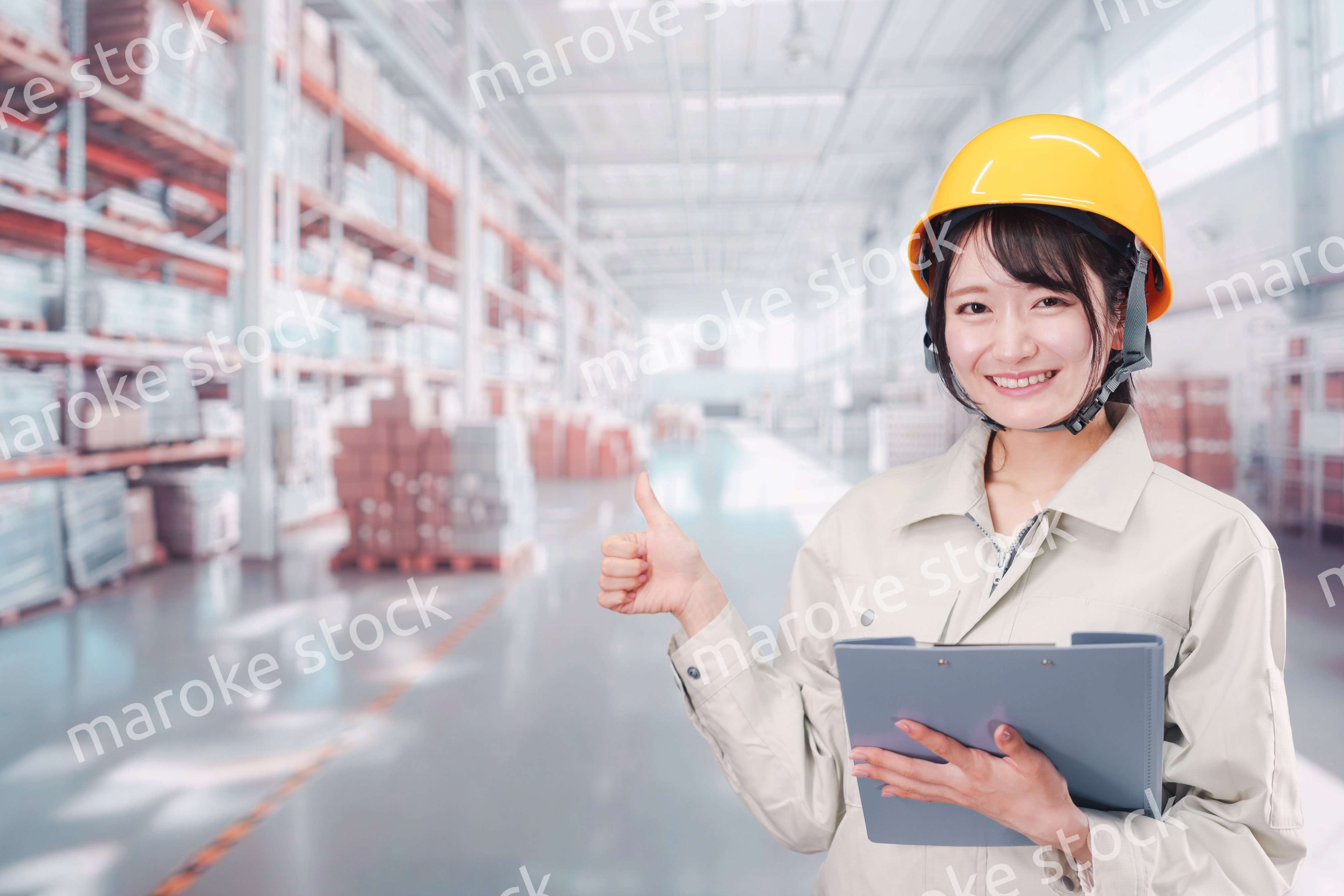 大きな物流倉庫で働くヘルメットを被った若い女性