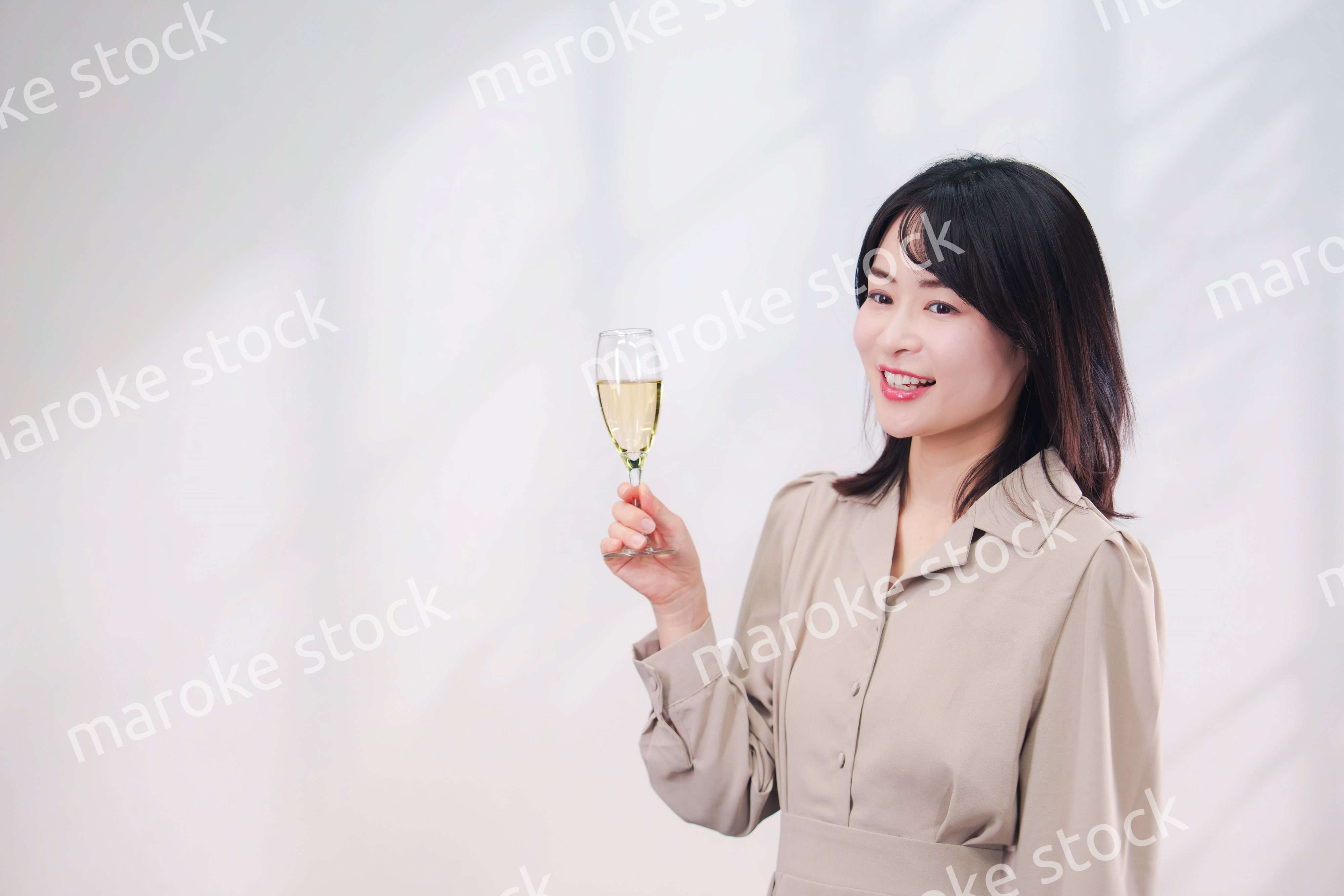 笑顔でスパークリングワインを飲む若い女性（シンプル背景）