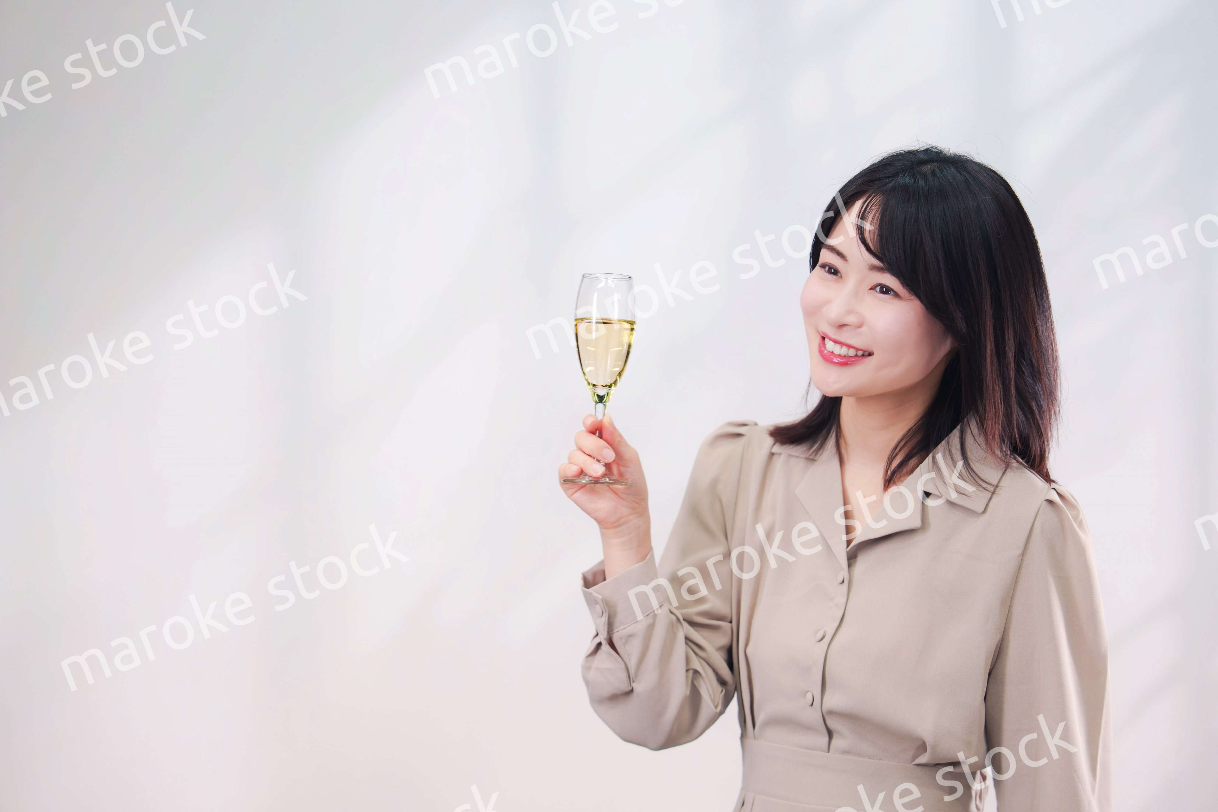 笑顔でスパークリングワインを飲む若い女性（シンプル背景）