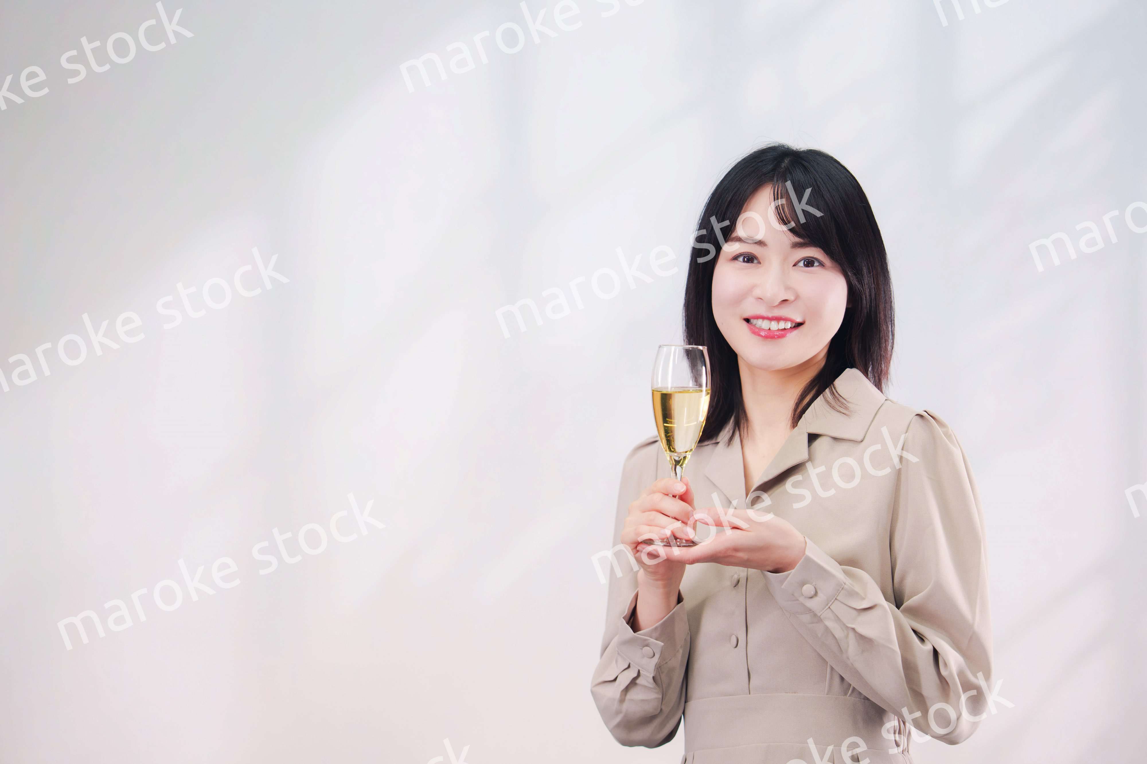 笑顔でスパークリングワインを飲む若い女性（シンプル背景）