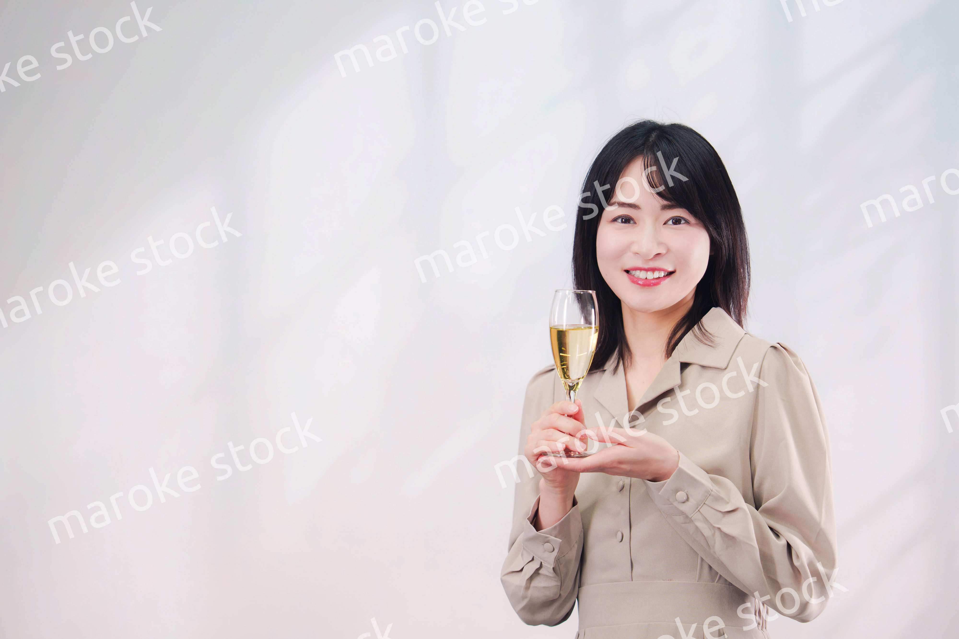 笑顔でスパークリングワインを飲む若い女性（シンプル背景）