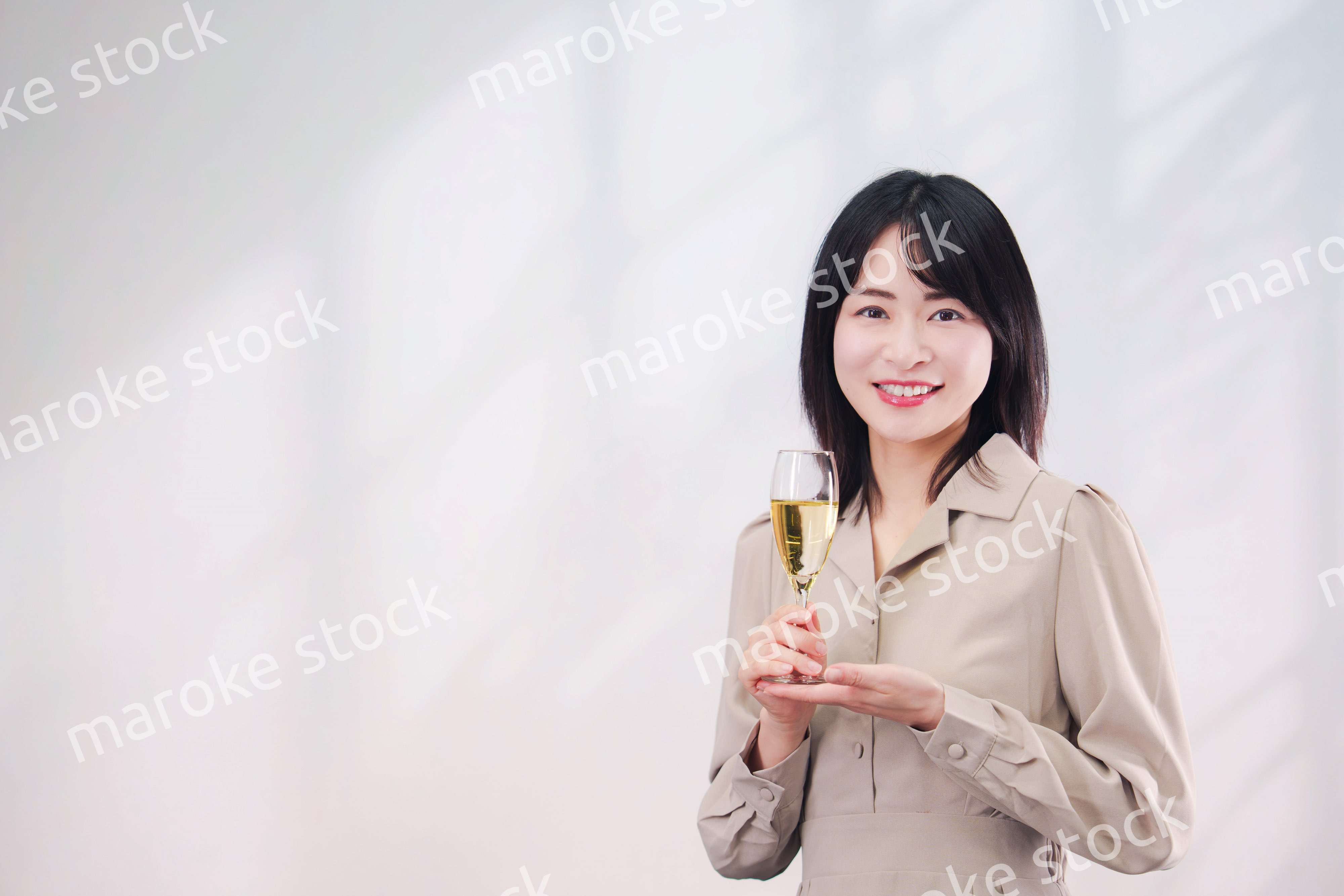 笑顔でスパークリングワインを飲む若い女性（シンプル背景）