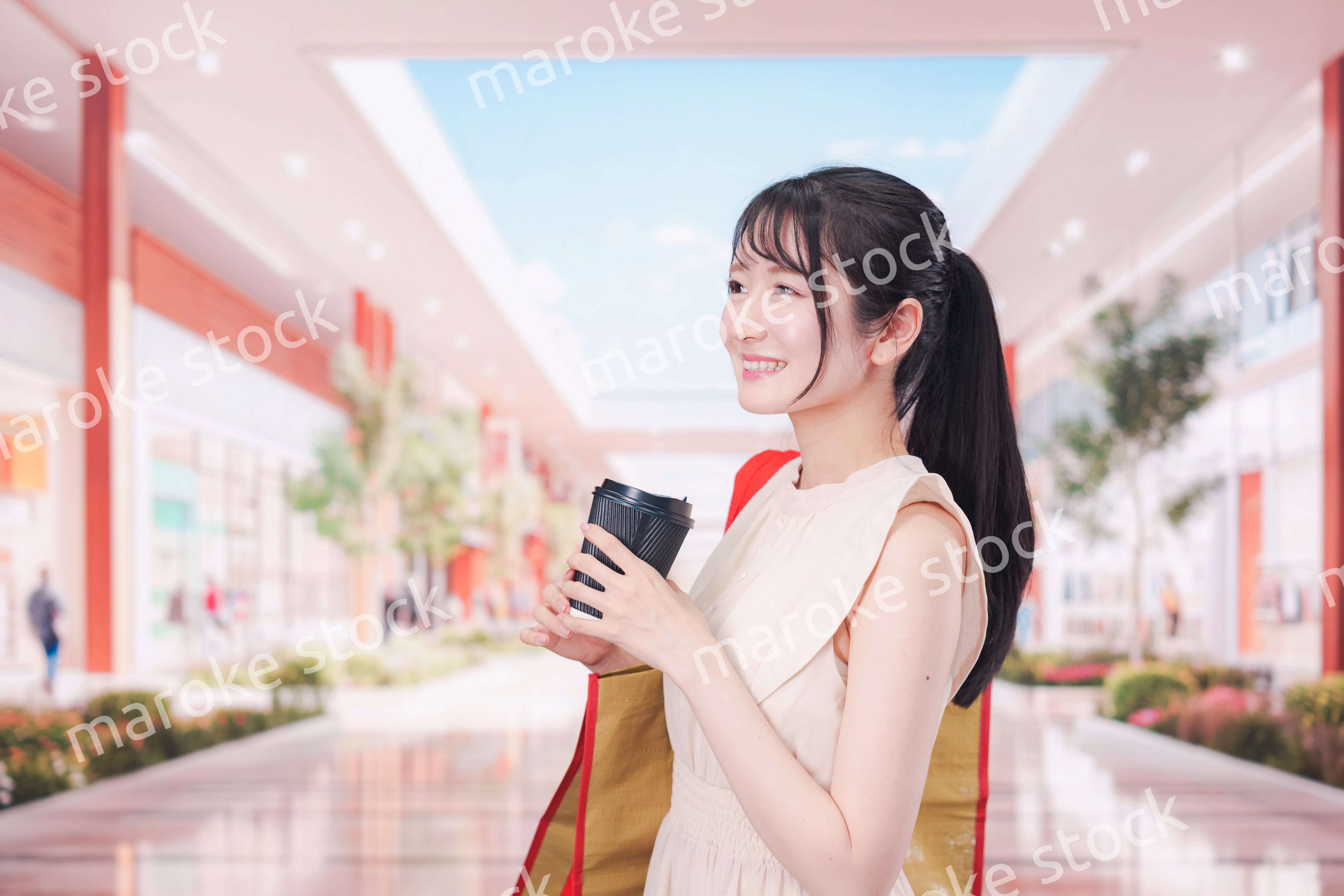 コーヒーを飲みながらショッピングモールで買い物をする女性