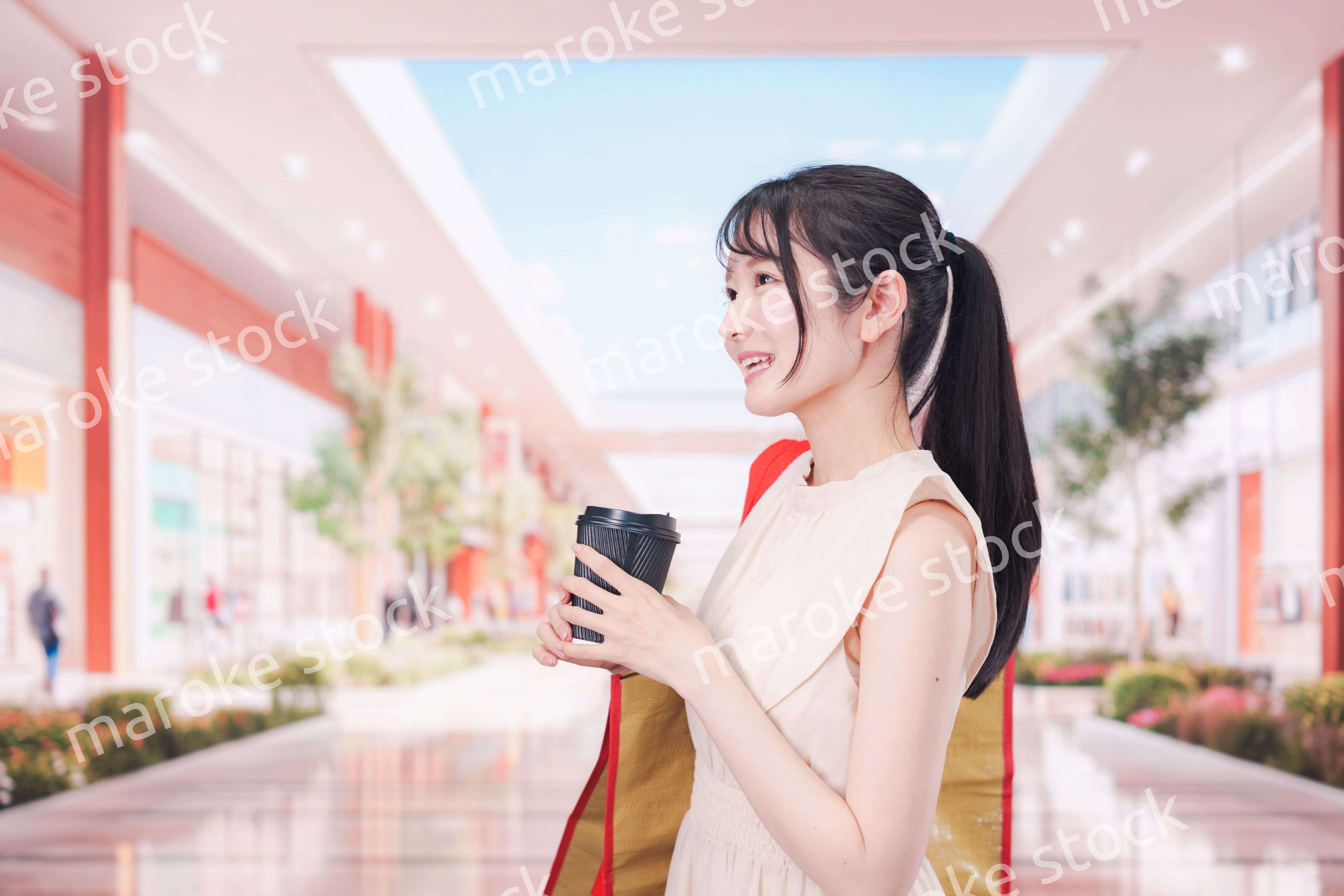 コーヒーを飲みながらショッピングモールで買い物をする女性