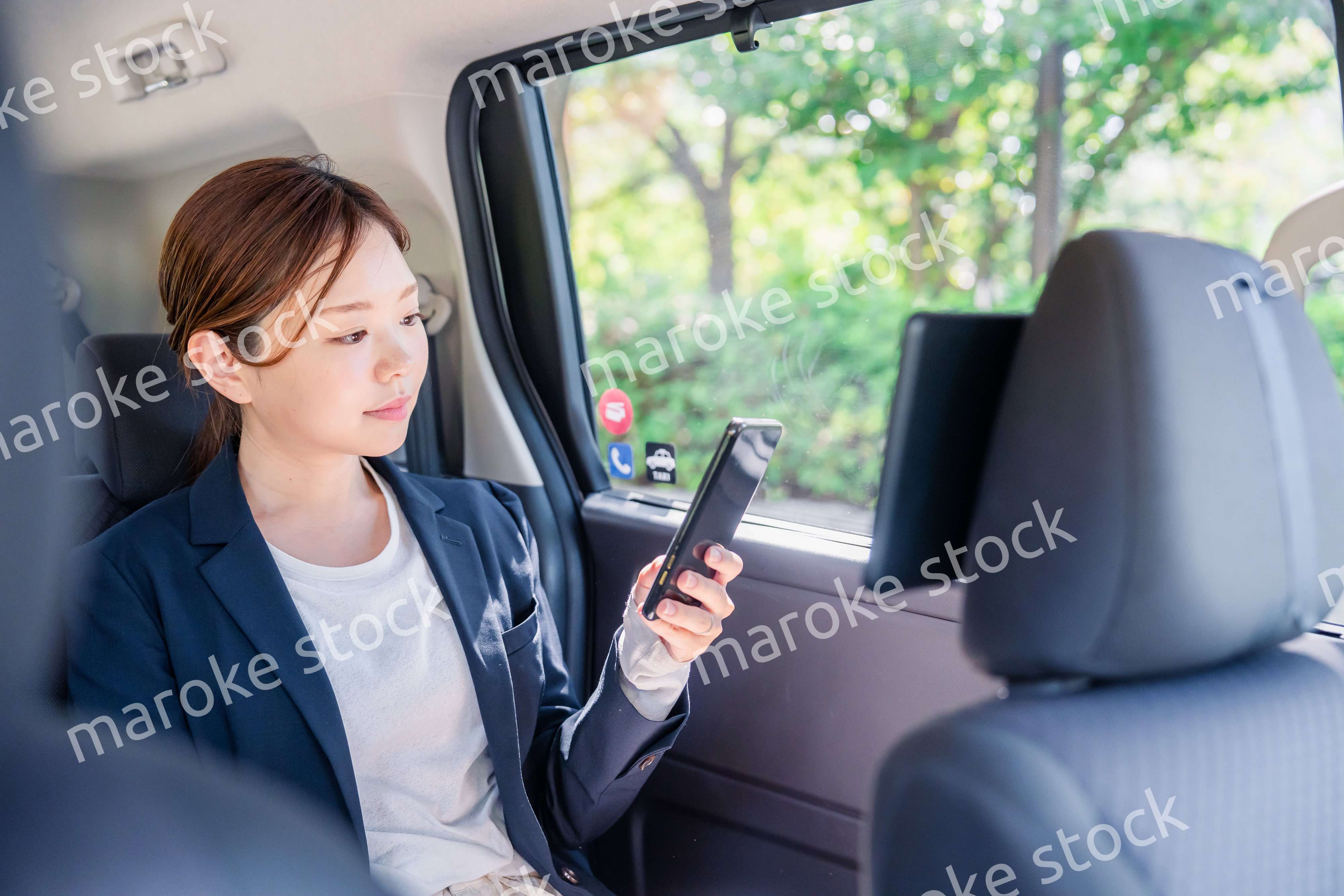 タクシーでスマホを使う若い女性ビジネスパーソン