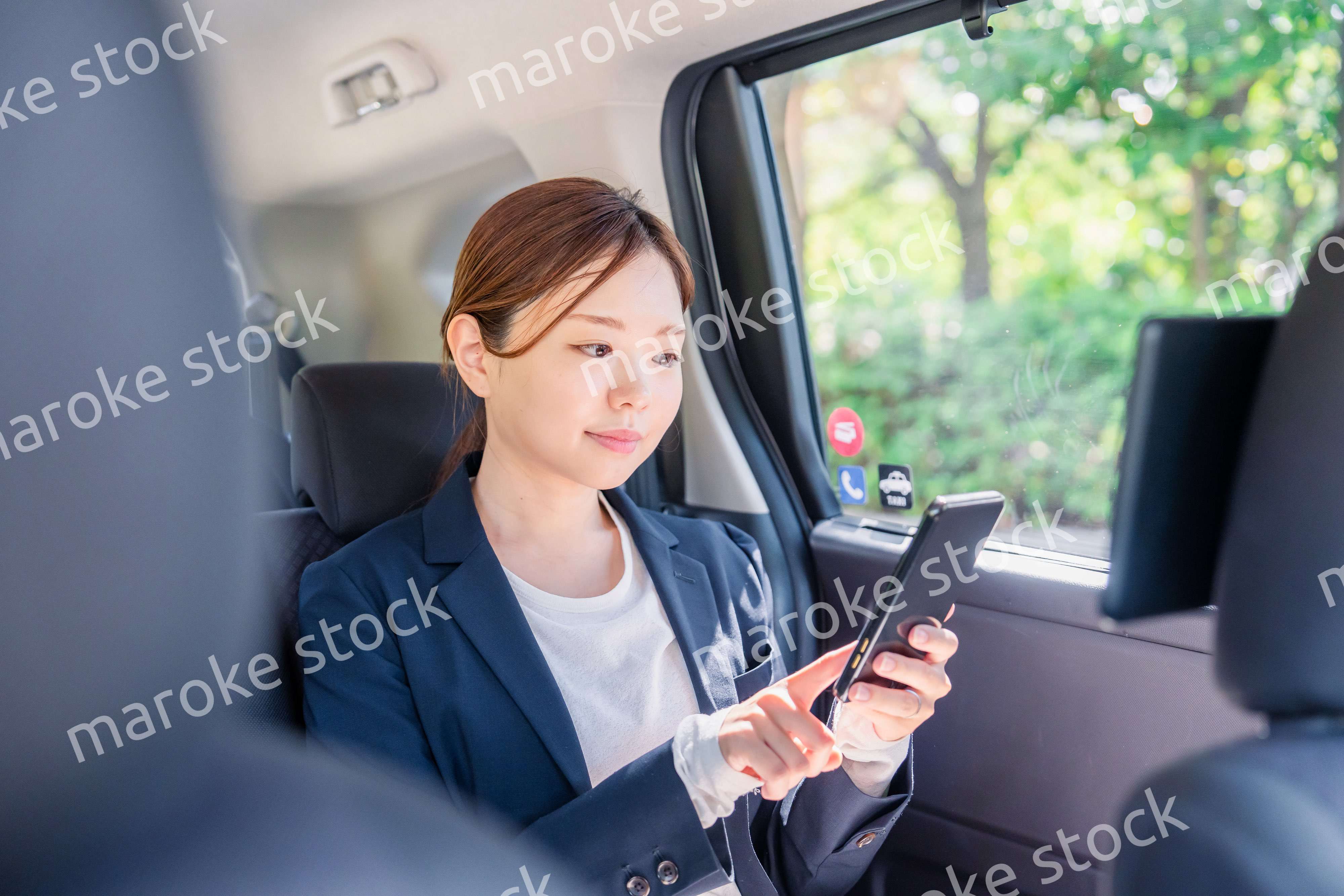 タクシーでスマホを使う若い女性ビジネスパーソン