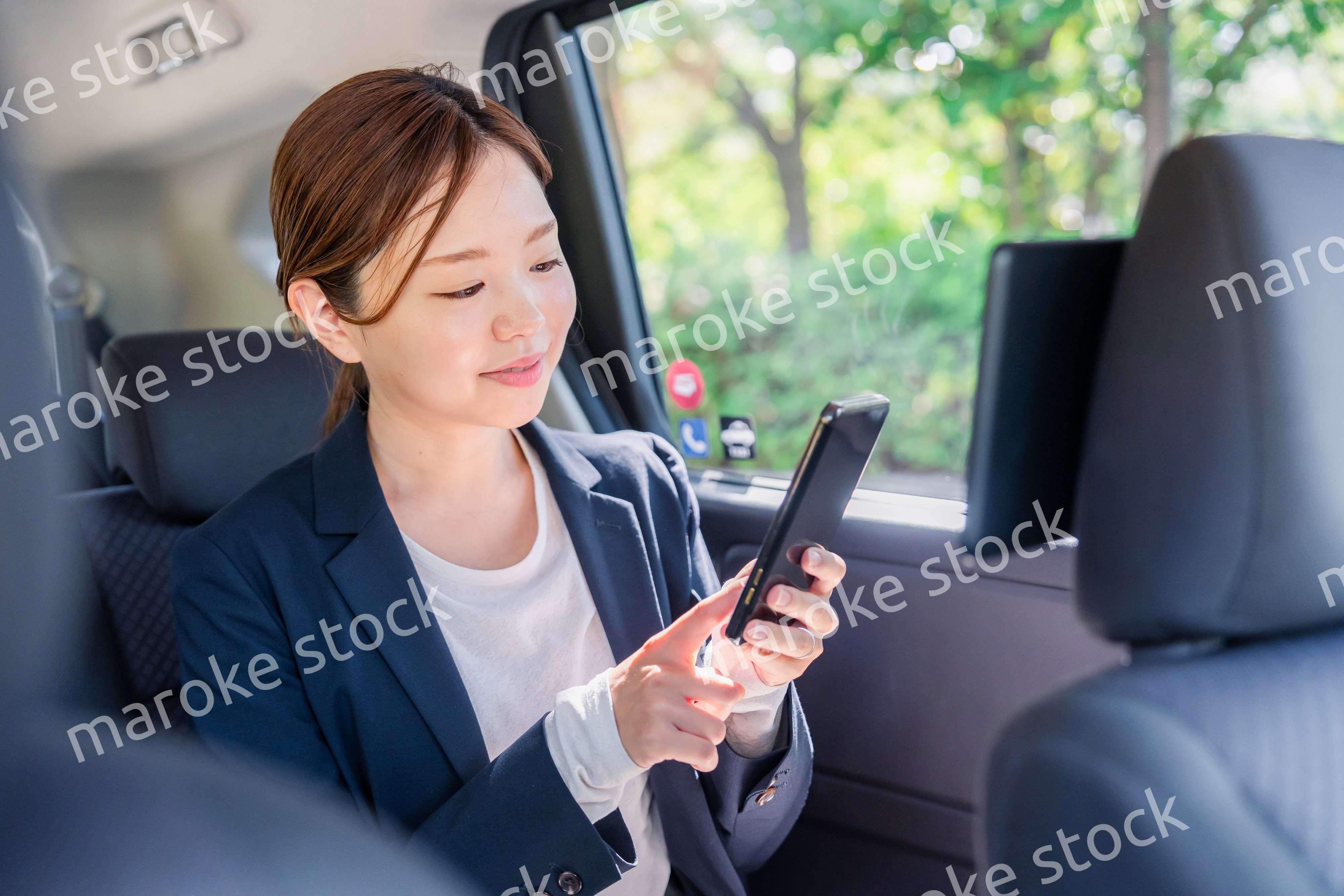 タクシーでスマホを使う若い女性ビジネスパーソン