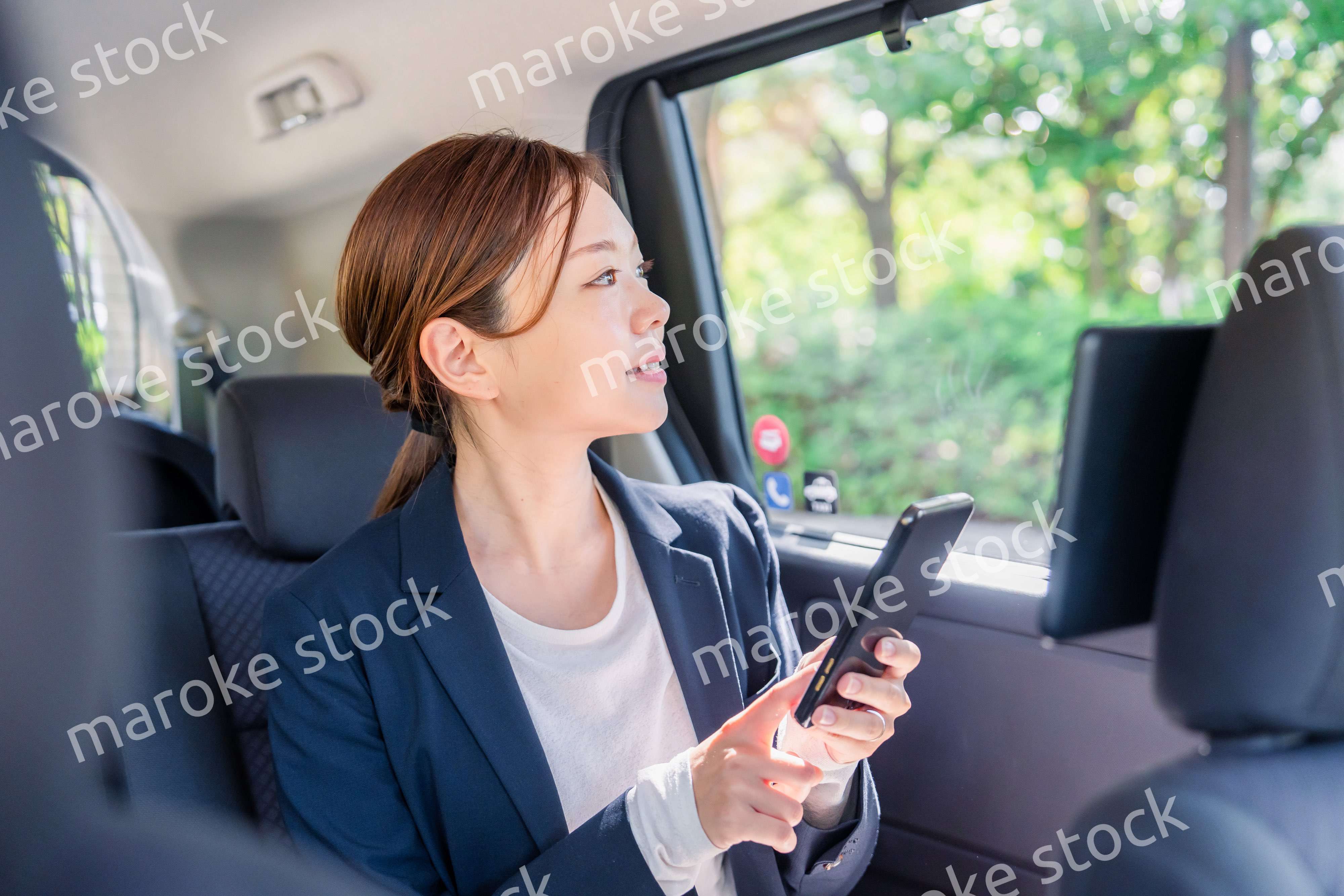 タクシーでスマホを使う若い女性ビジネスパーソン