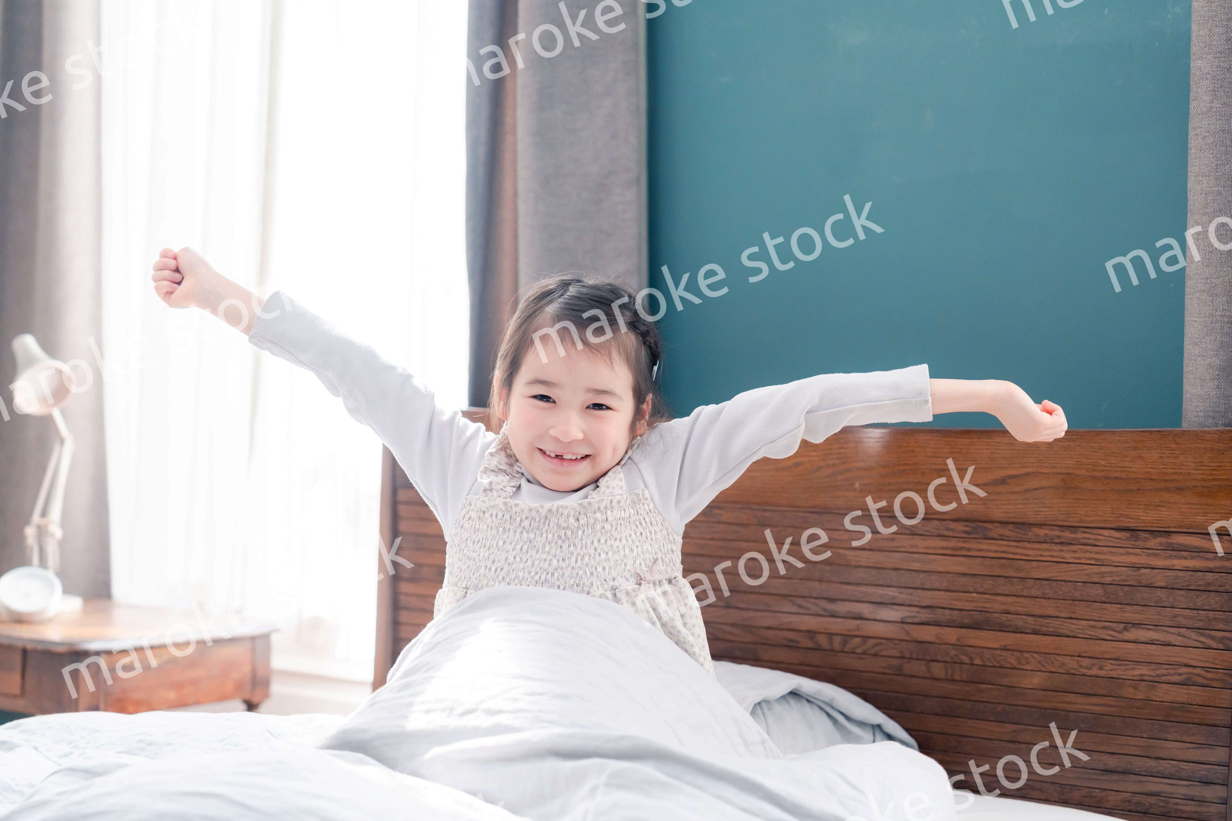 朝ベッドで目覚めて伸びをする小さな女の子