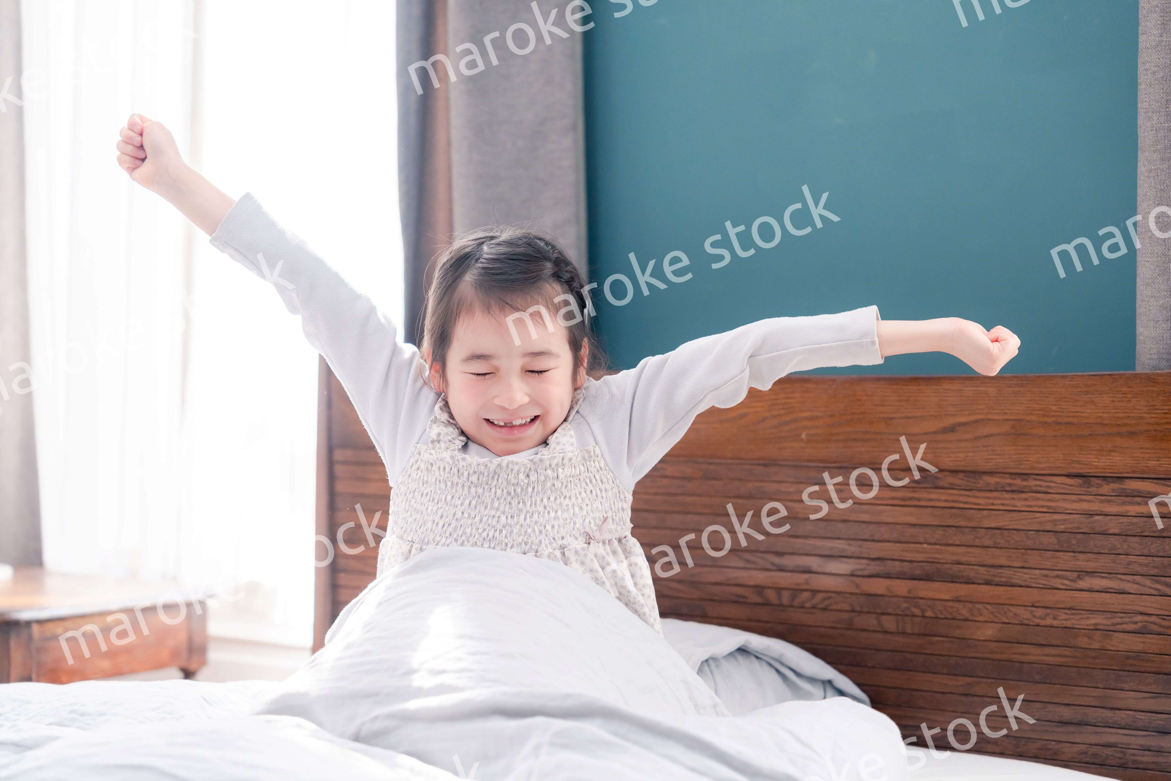 朝ベッドで目覚めて伸びをする小さな女の子