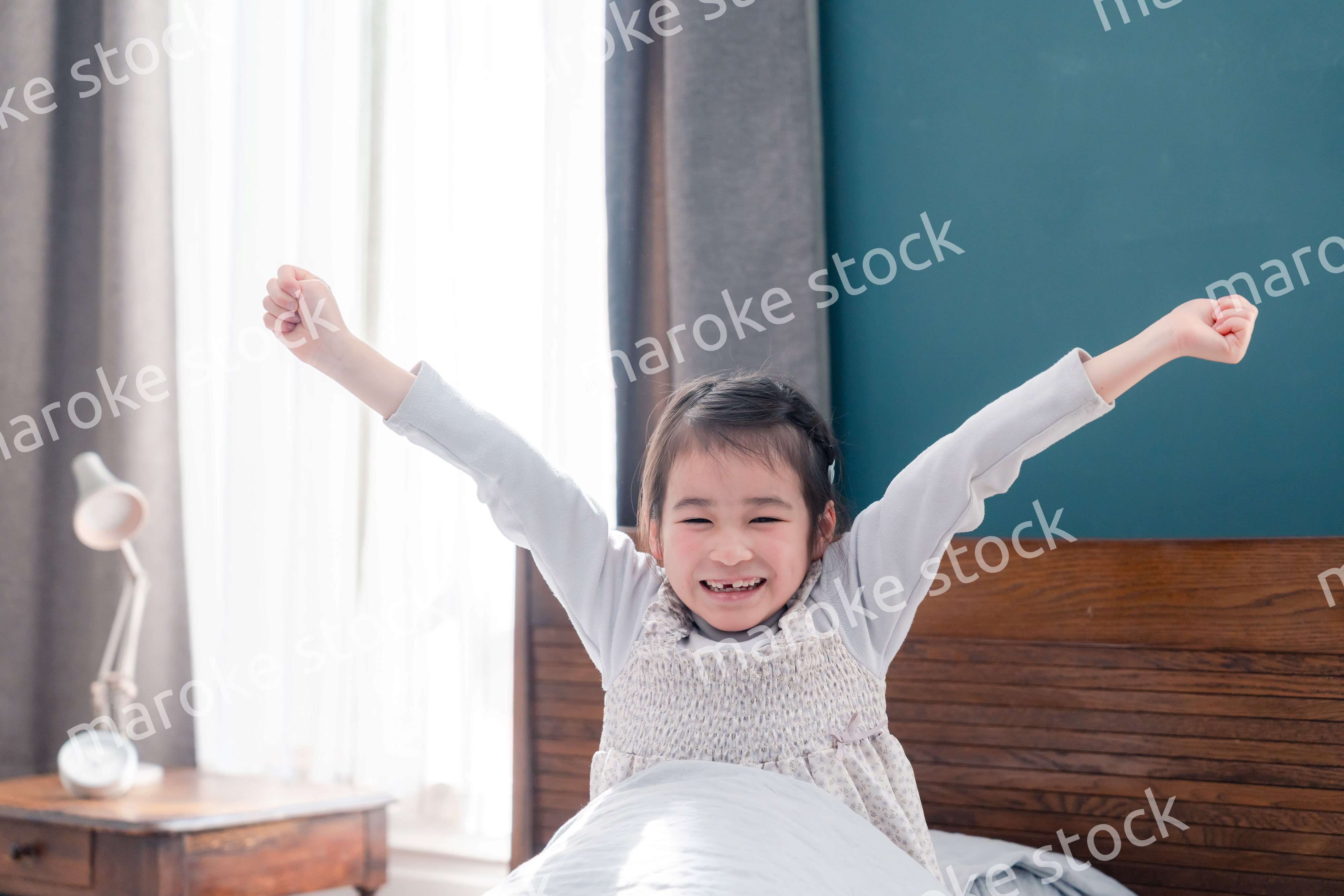朝ベッドで目覚めて伸びをする小さな女の子